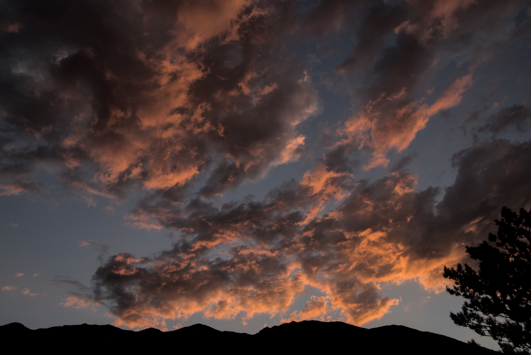 Fragmented clouds turn pink with the sunset over a high mountain ridge.