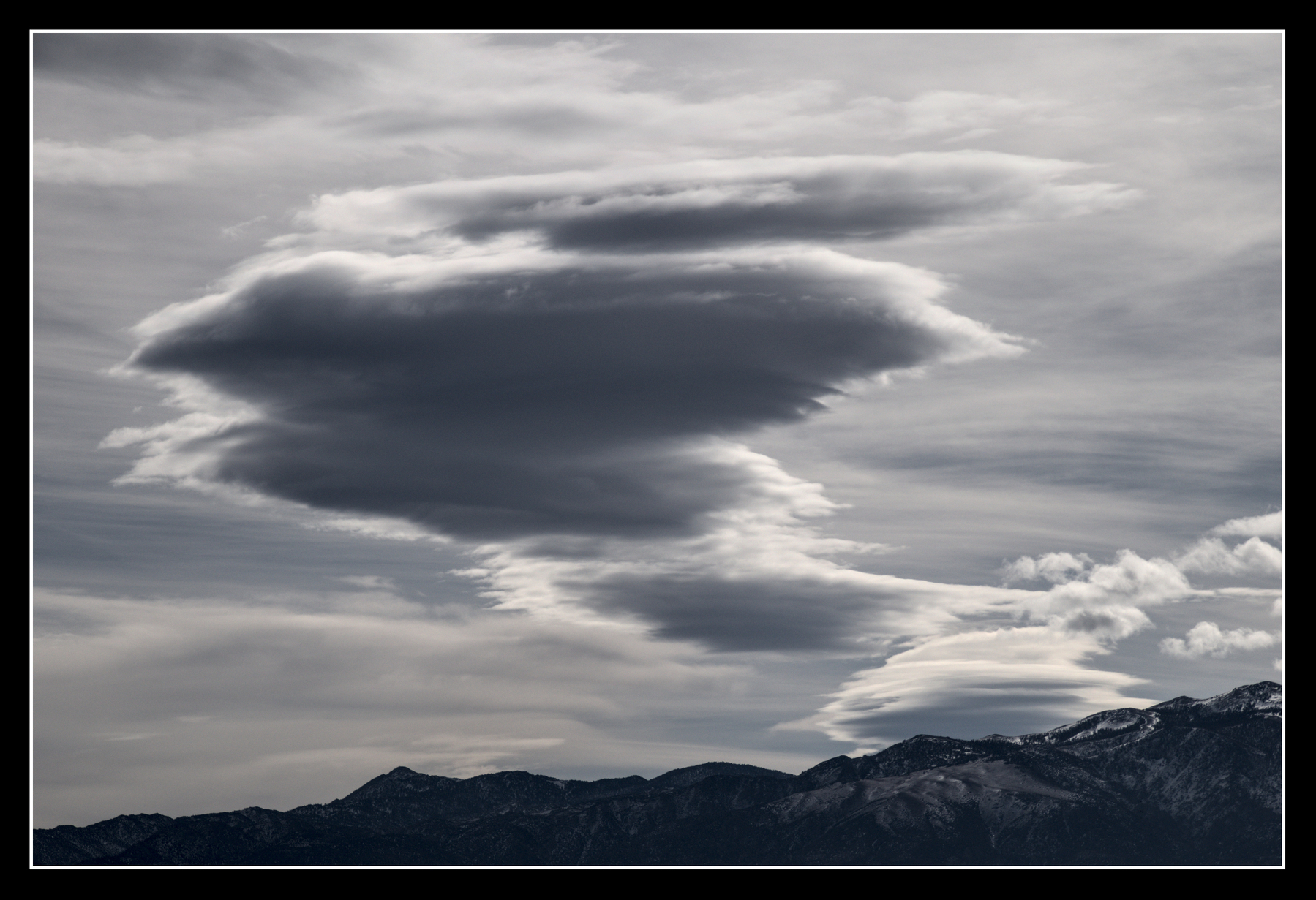 A lenticular cloud rises from a mountain, growing wider as it rises and zig-zags, making it look like a classic genie emerging from a bottle.