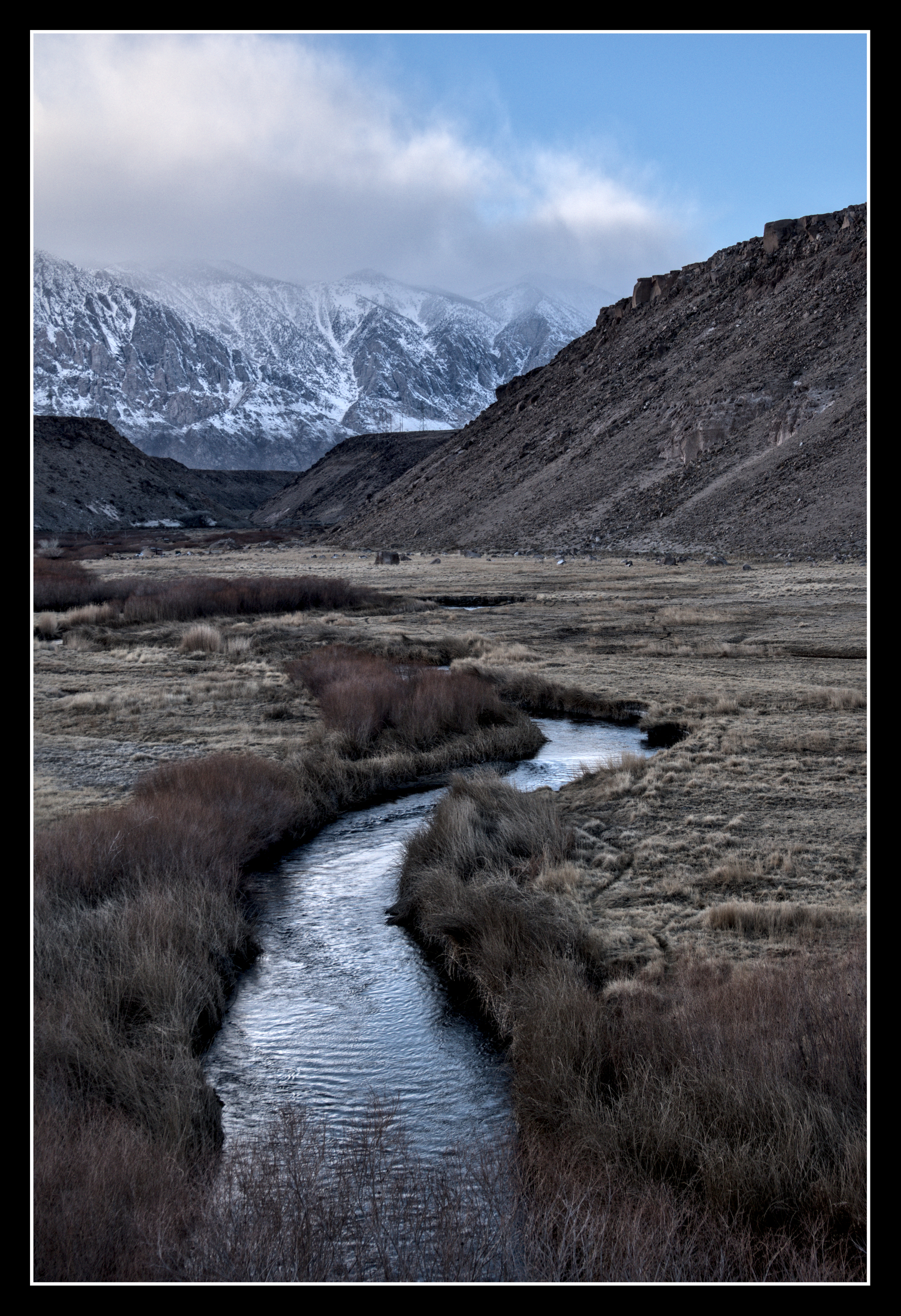 A river cuts through a grassy valley.  Upstream are pink, rocky bluffs.  Beyond them, snow-capped granite mountains.
