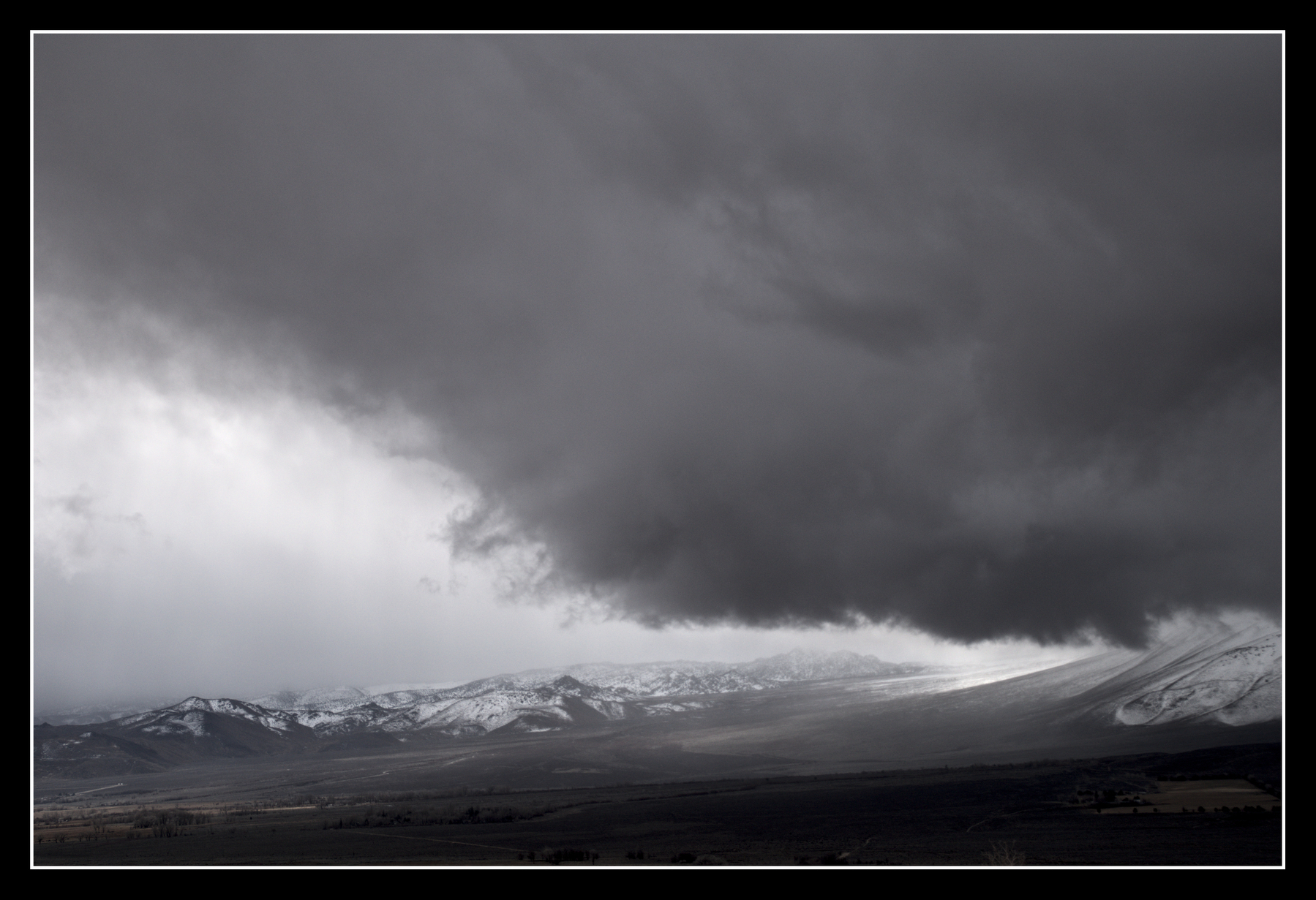 The tail of a mountain slopes from right to left, dwarfed by a large, dark cloud hovering over it.