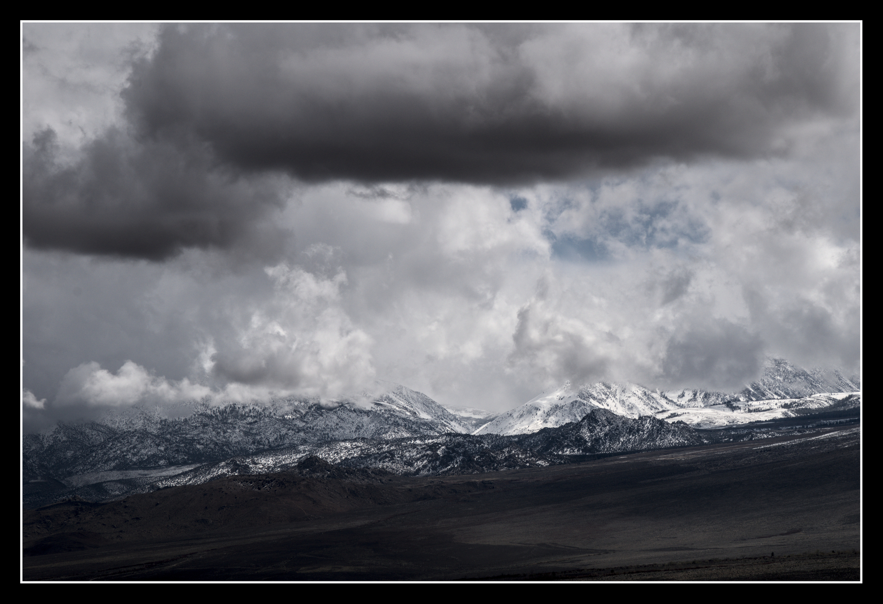 A variety of clouds, some light, some dark, over a low range of mountains.