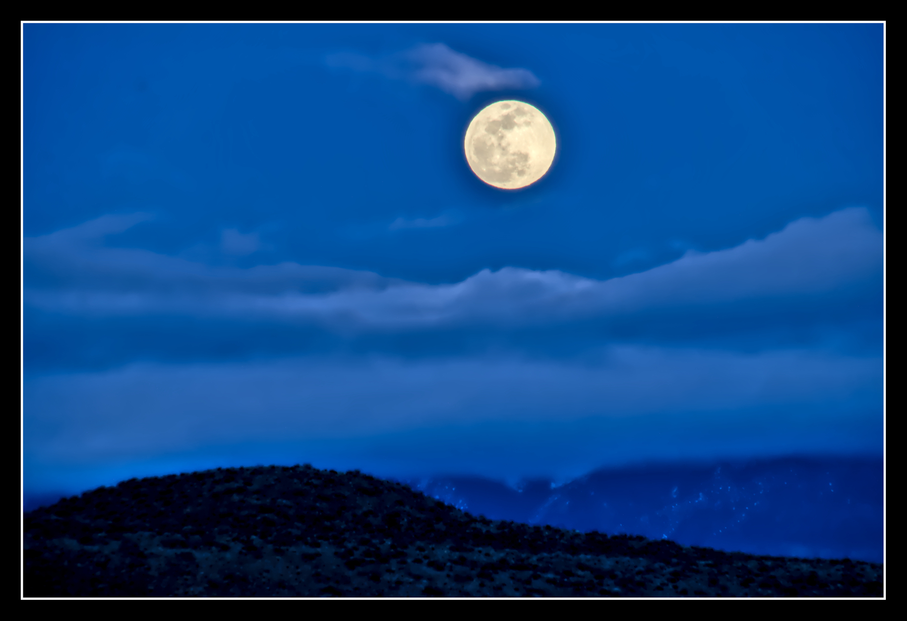 Moonrise, the moon is full and white, while the landscape is blue with evening light.
