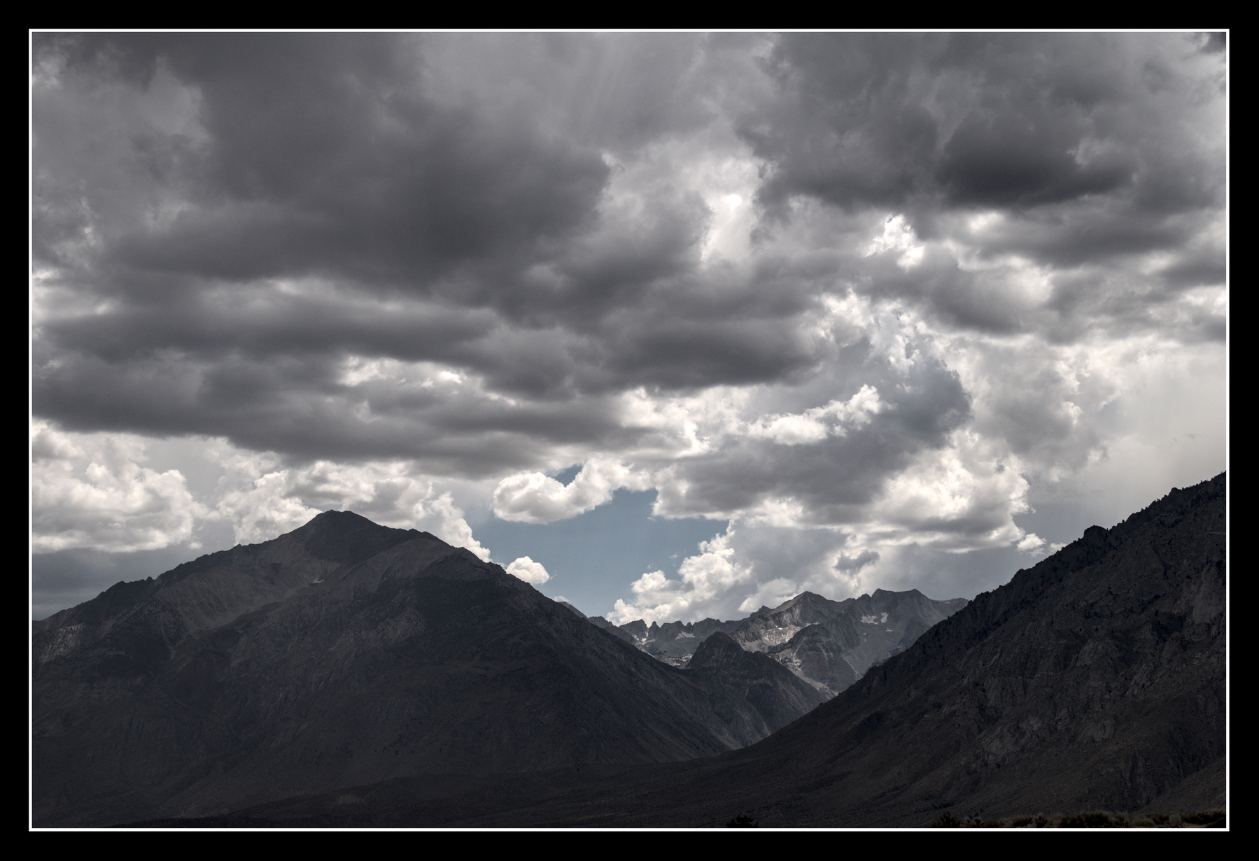 A dark cloudy sky rises from jagged  mountains.