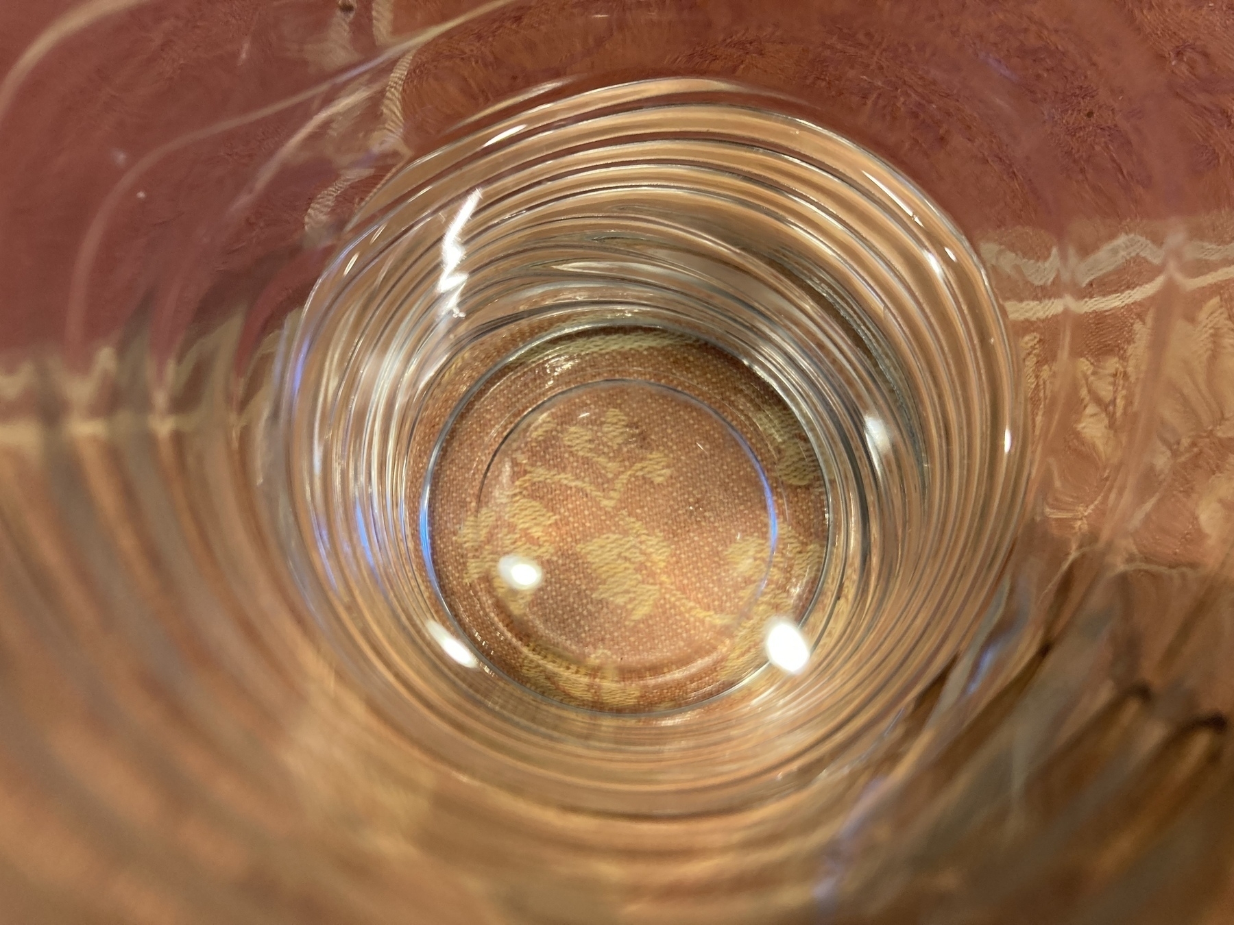 The camera lens looks straight down into a ribbed glass half full of water sitting on a tablecloth.