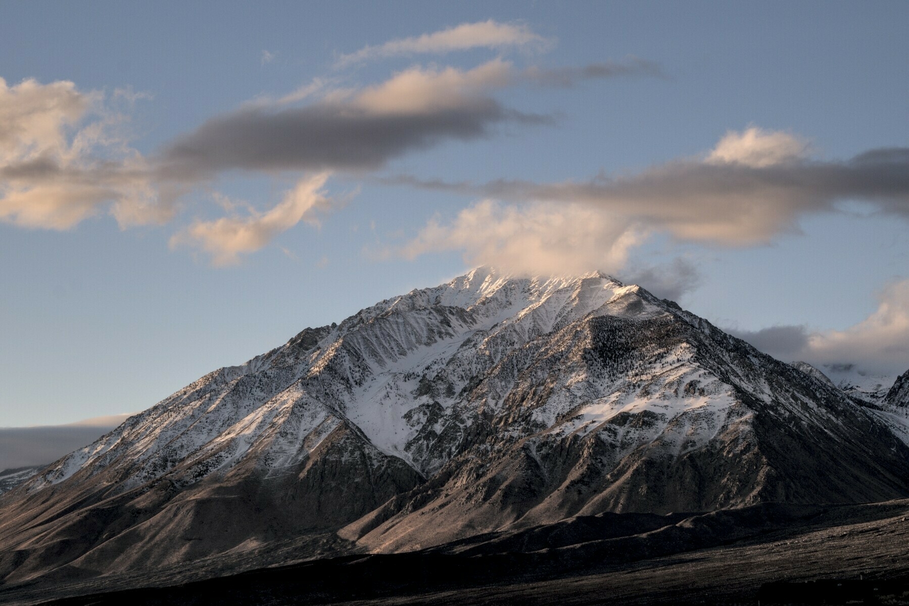 A craggy triangular mountain has a motley group of clouds floating past it.