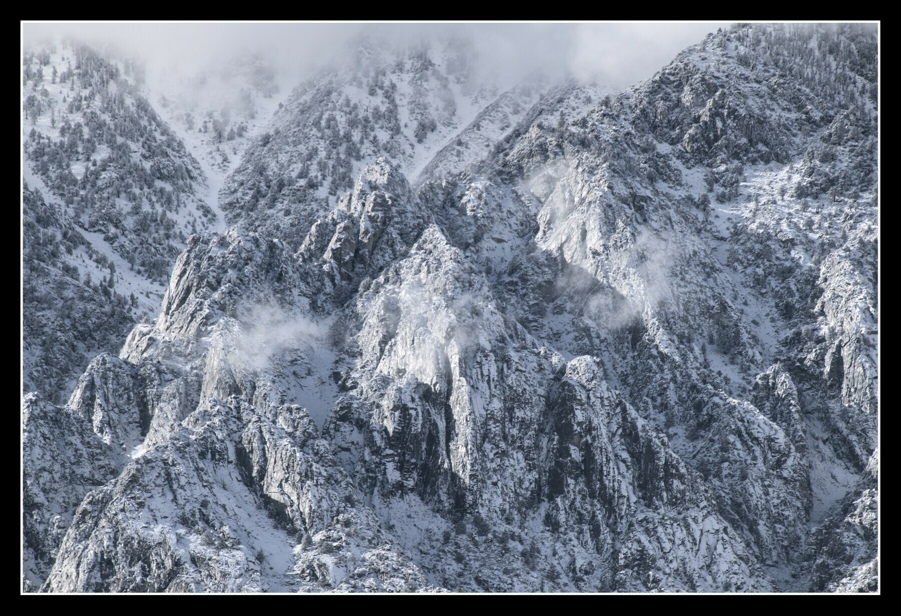 Jagged granite outcrops on a large mountain wall are covered with fresh snow.