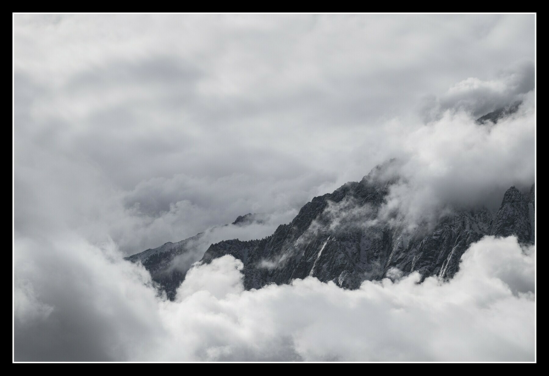 A granite mountain ridge is only partially visible through a variety of cloud banks.