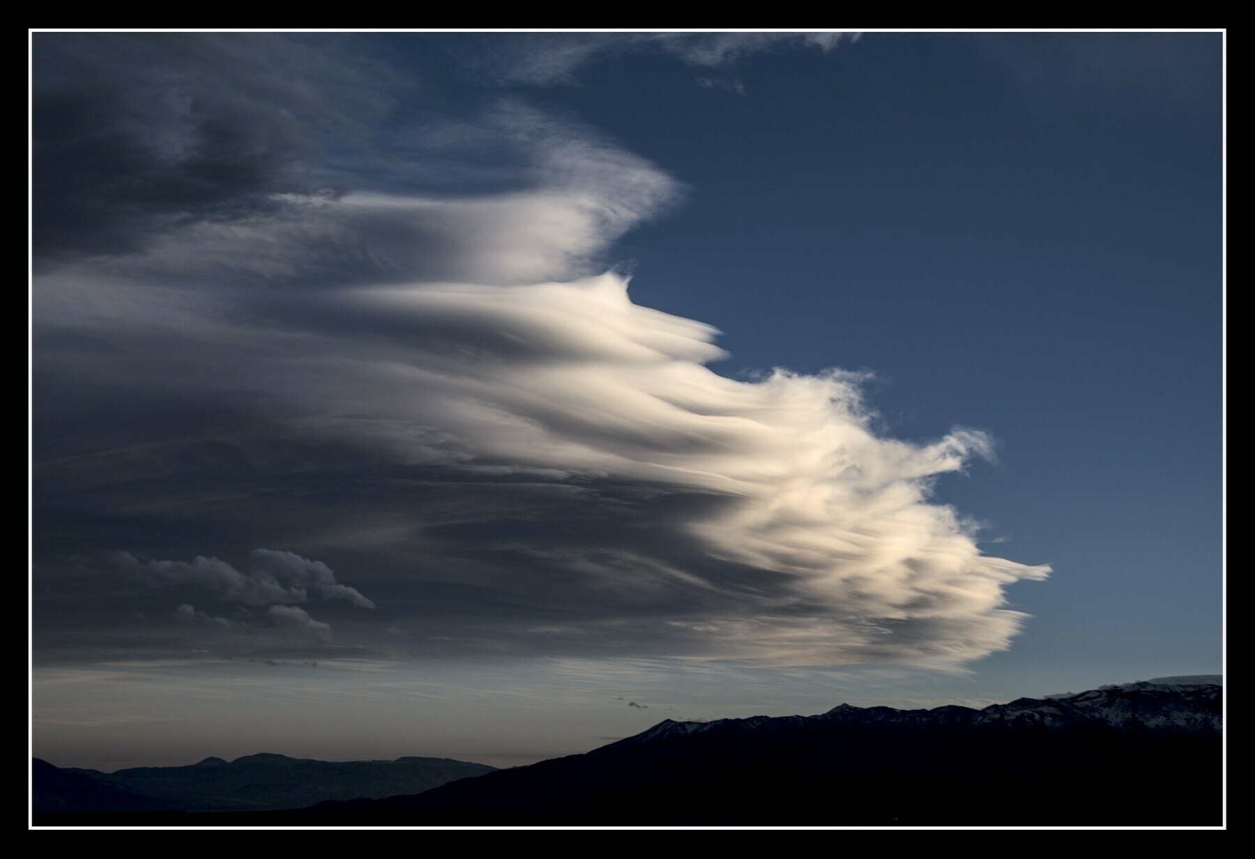 A sculpted cloud hovers over mountains.