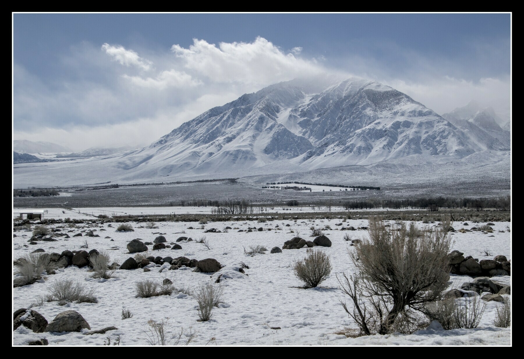 A triangular snow-covered mountain rises above a high desert valley.