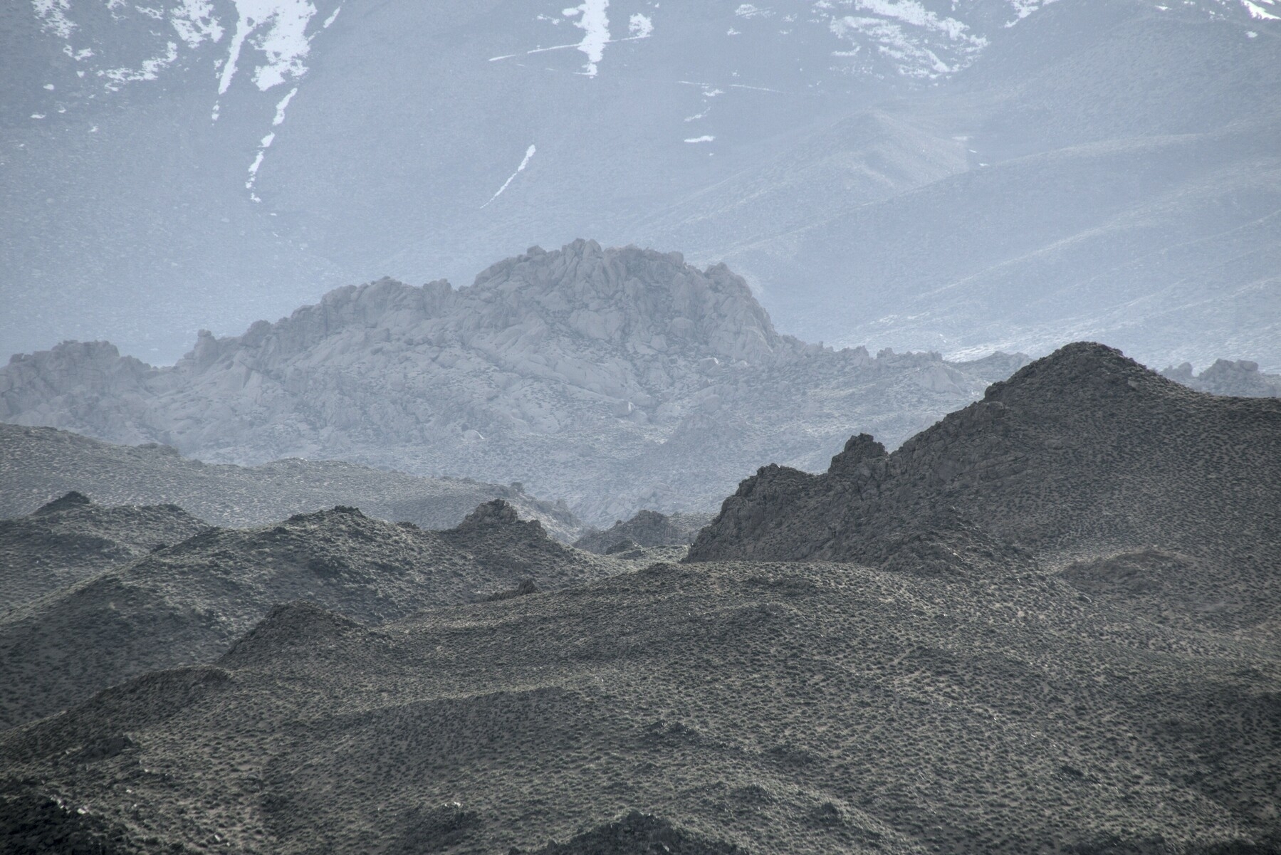 Rocky foothills have no vegetation on them, with snow visible on the mountains behind.