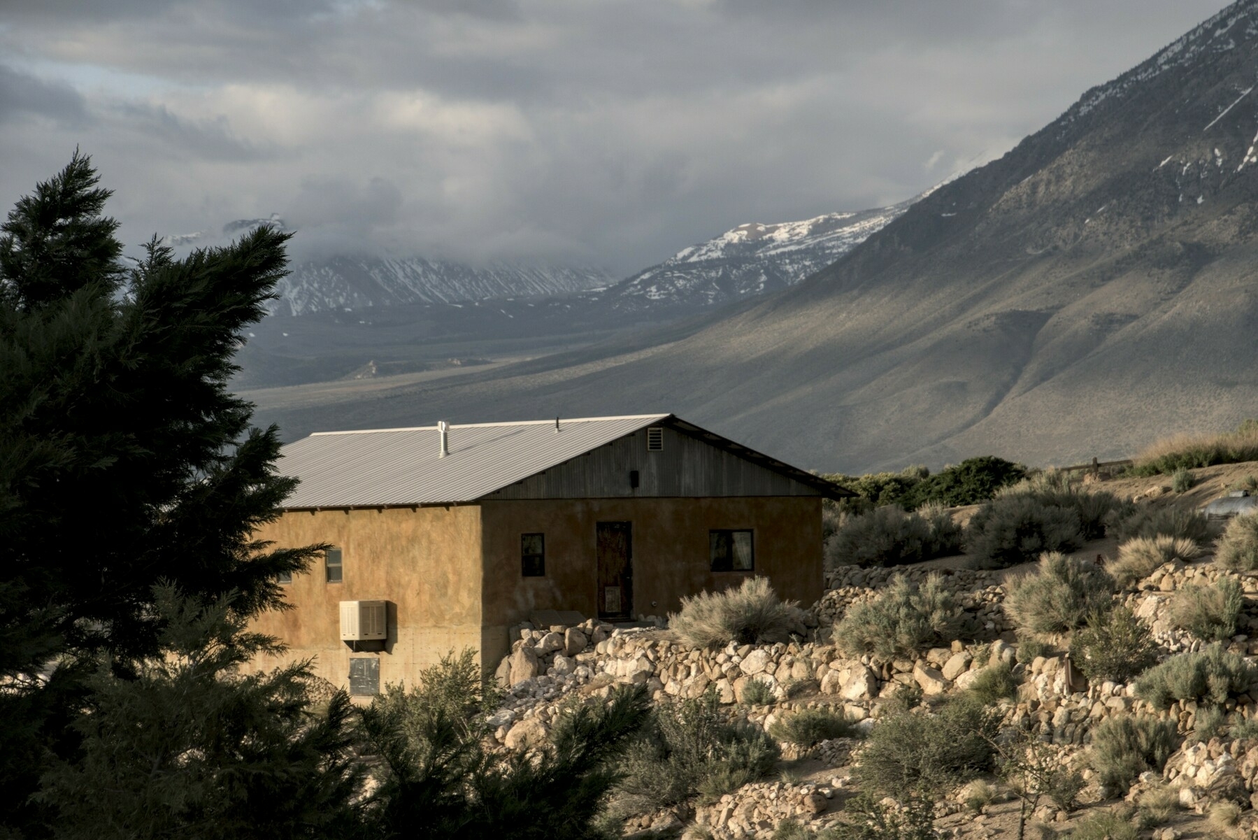 A small house is lit by the setting sun, with mountains behind.