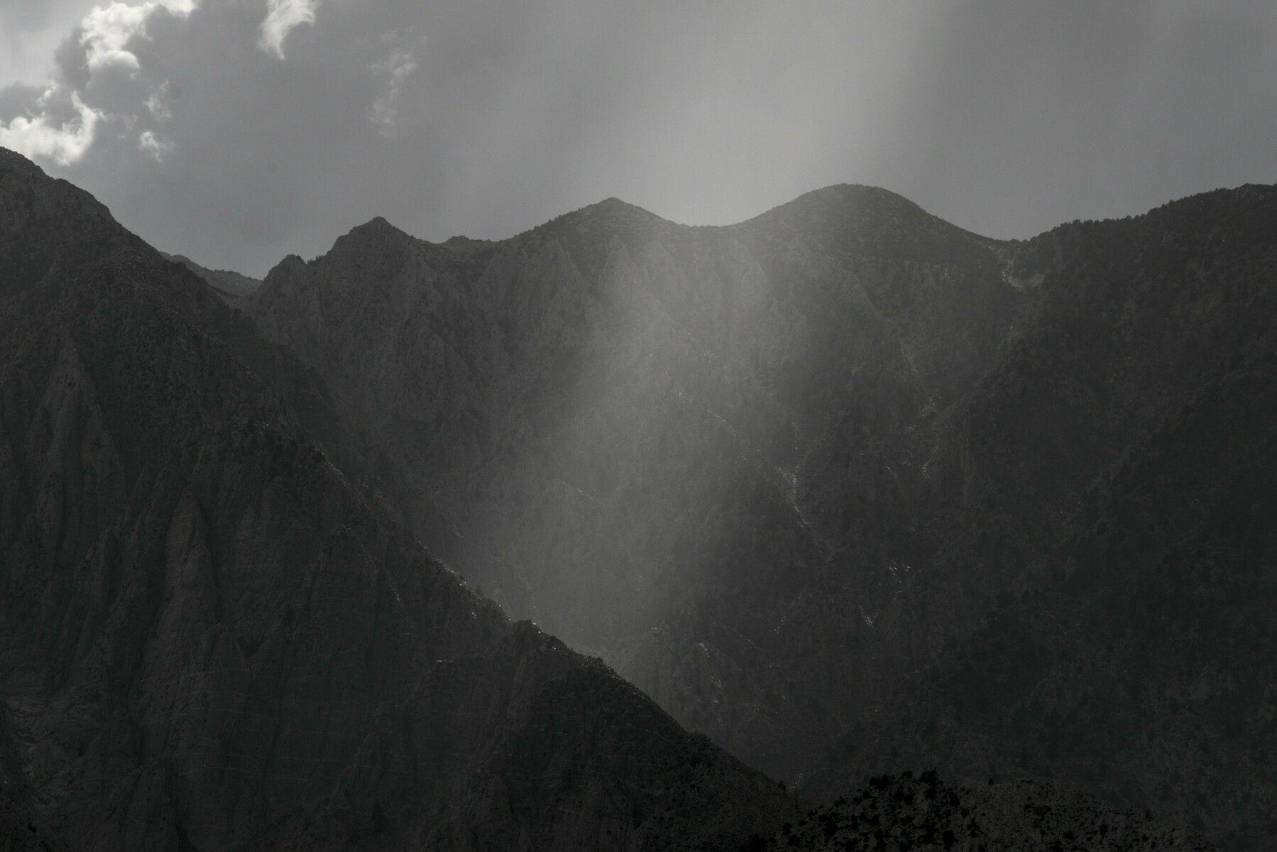 A cone of light breaks through the clouds over a mountain valley.