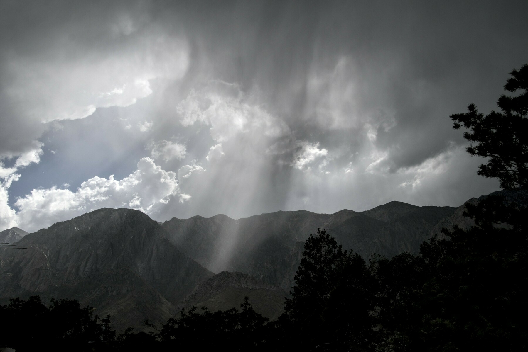 Light shines in beams through cloud and haze over a mountain  range.