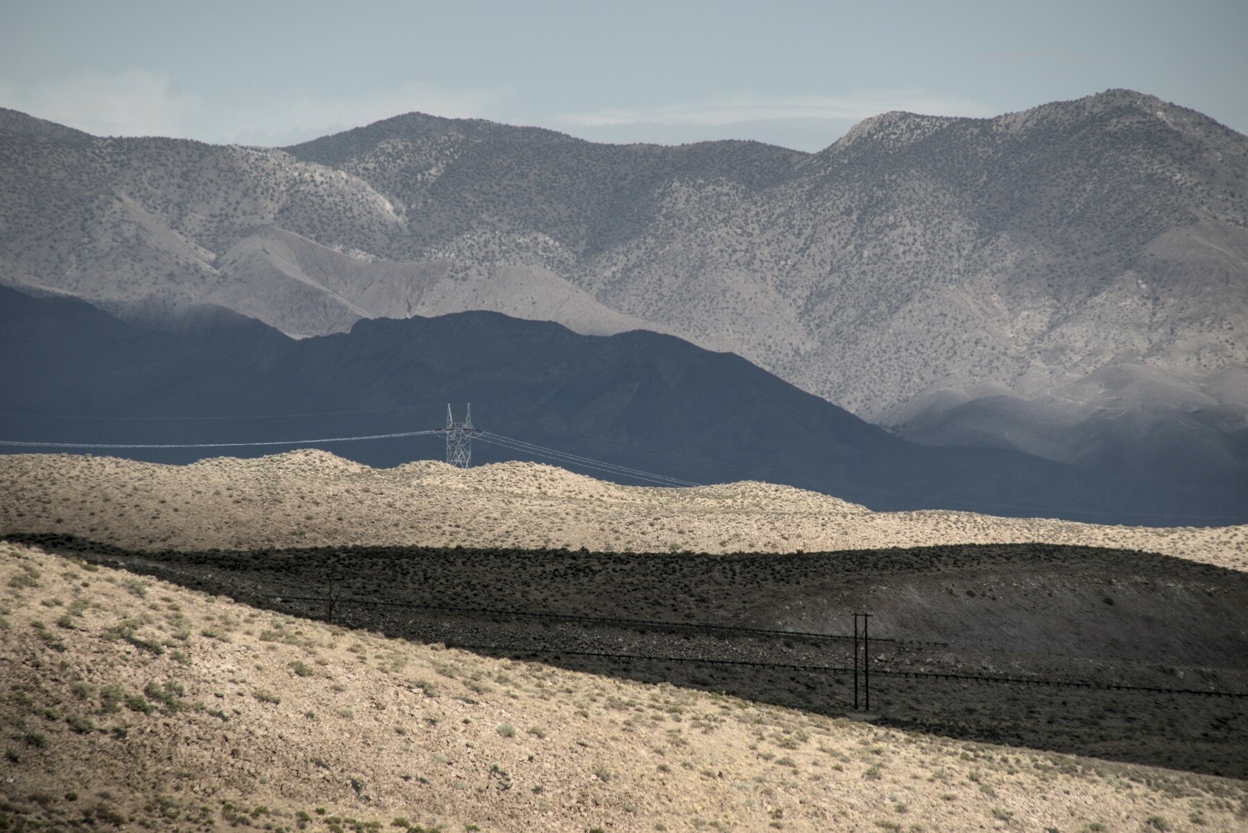 A high desert landscape, with mountains in the distance, is alternately in sun and shadow, making strong bands and wedges of land distinctly visible.