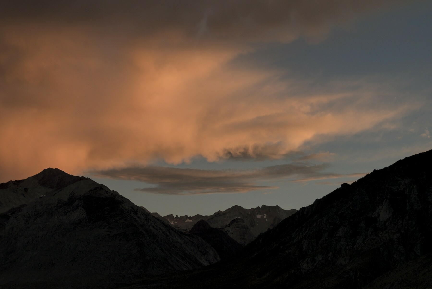 Clouds lit dimy by the fading sunset hover over mountain silhouettes.