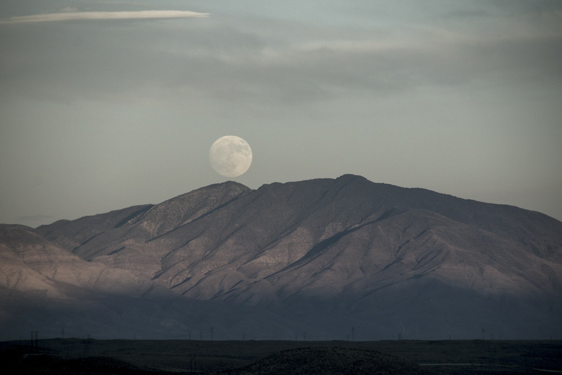 The rising full moon appears to be resting on the tip of a mountain.