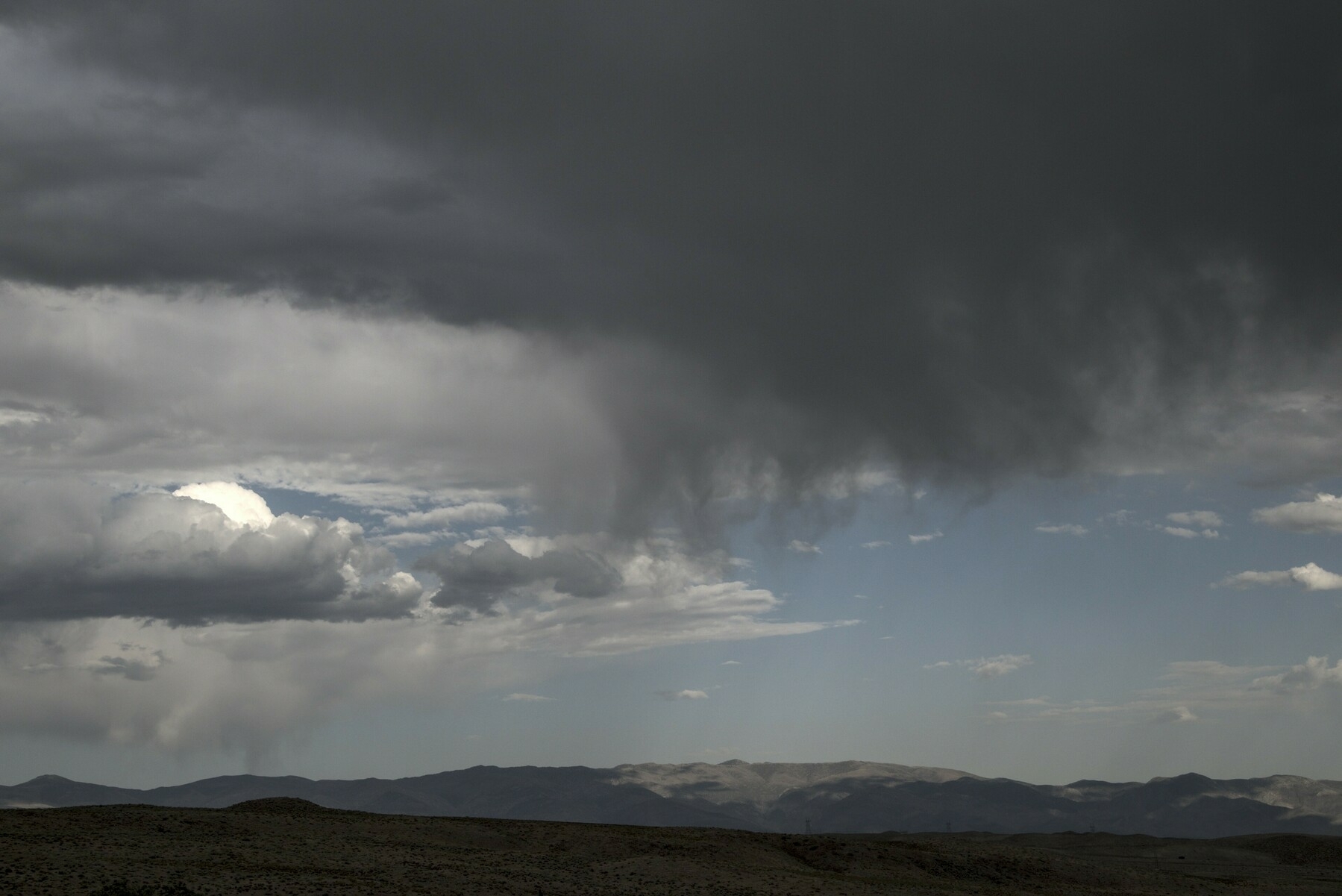 Dark rain clouds over dry mountains let a dark curtain of rain fall, curled by the wind.