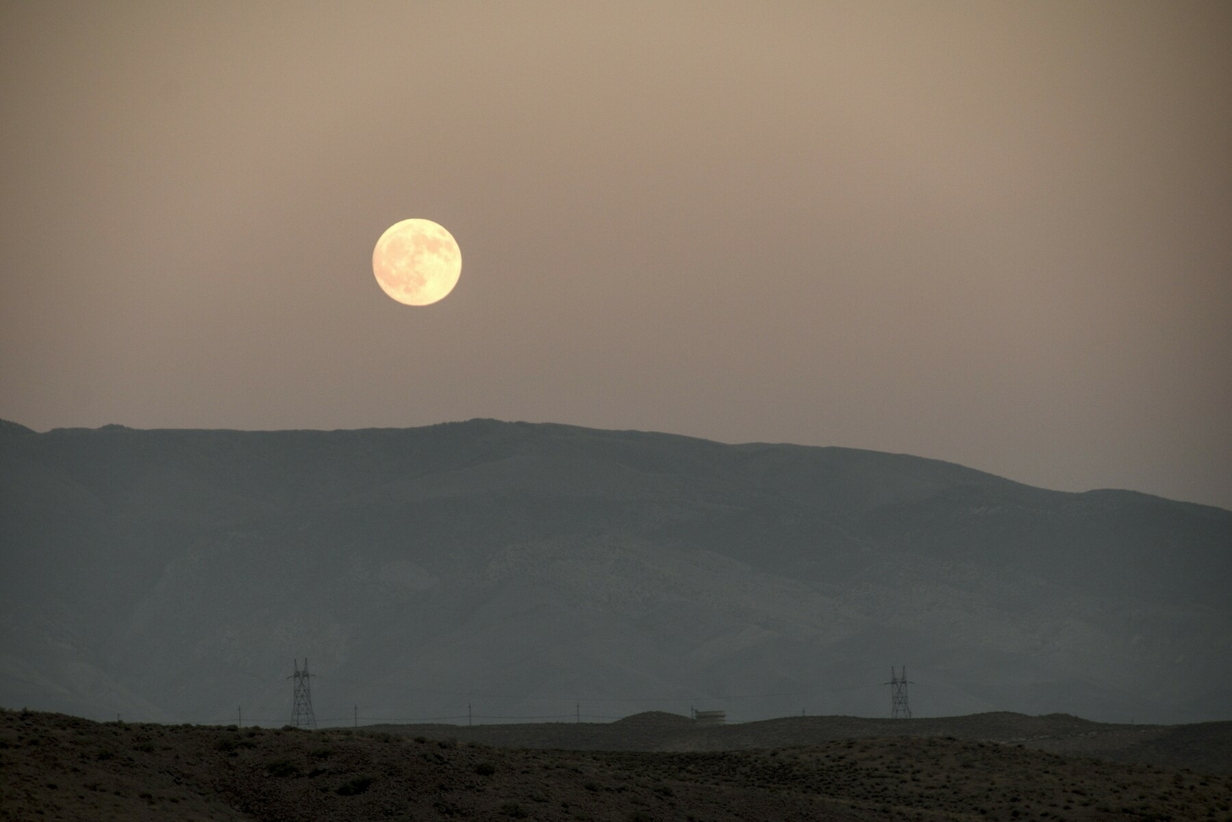 The full moon rises over mountains blurred and discolored by smoke.