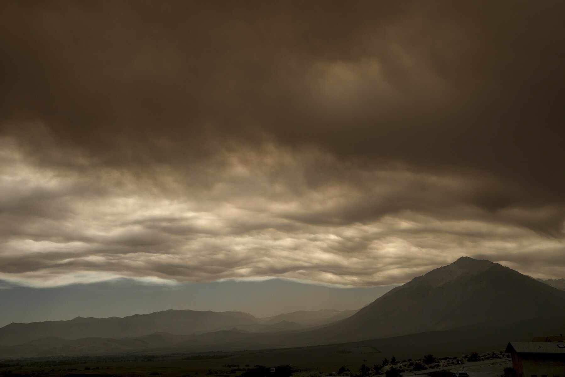A layer of dark smoke floats over a mountain valley.