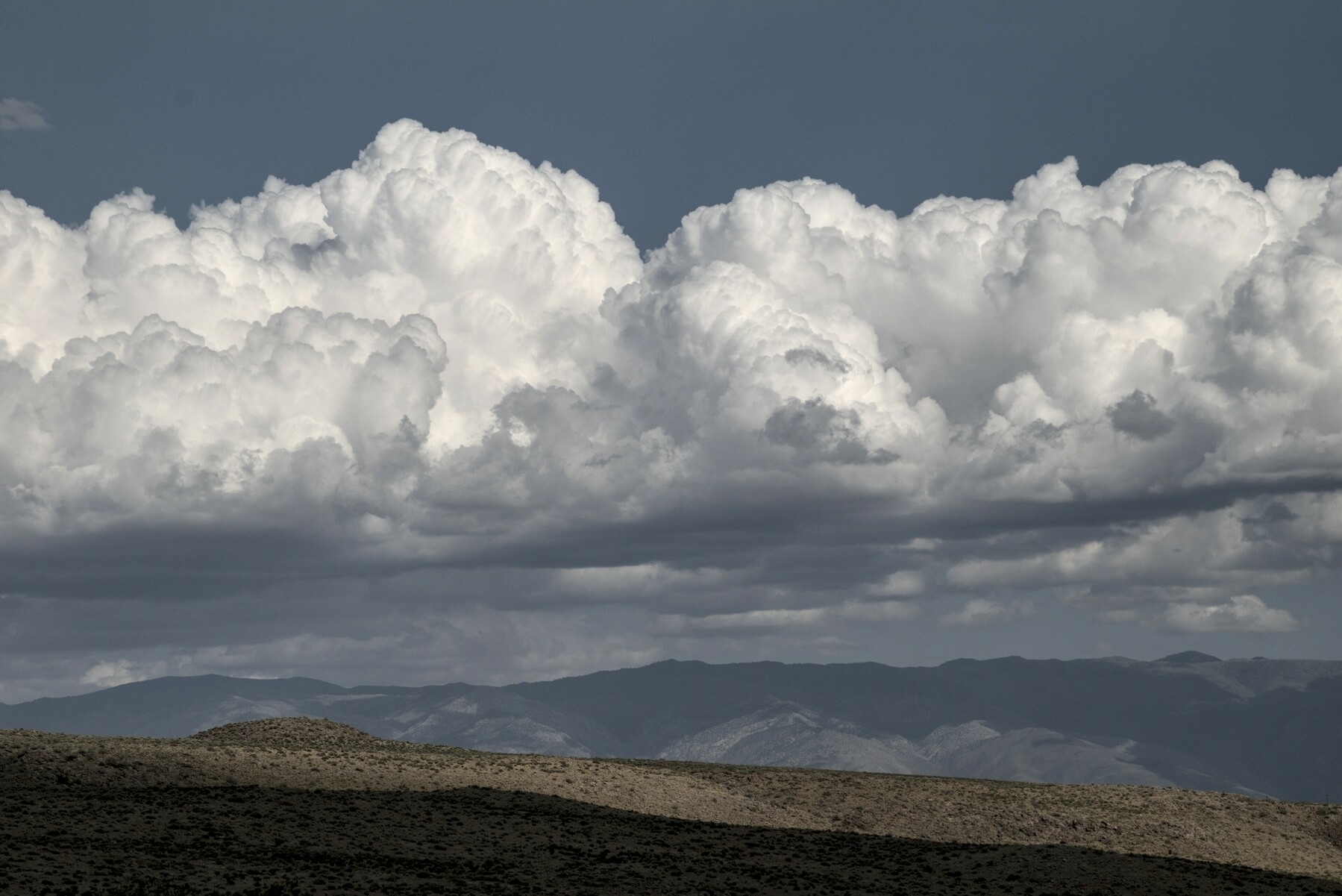 A large bank of fluffy white clouds floats over a long mountain range.