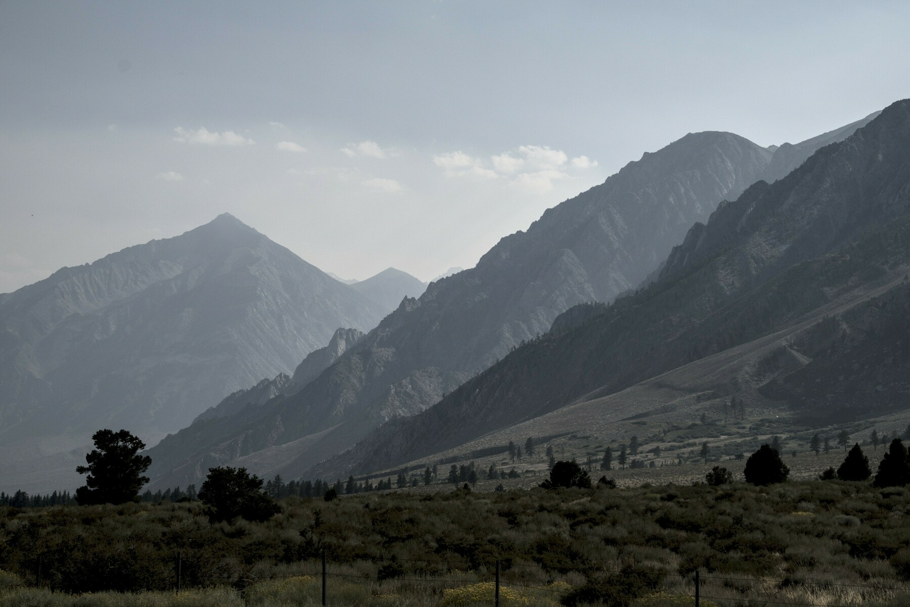 A mountain wall recedes in shades of gray as wildfire smoke gets dimmer in the distance.