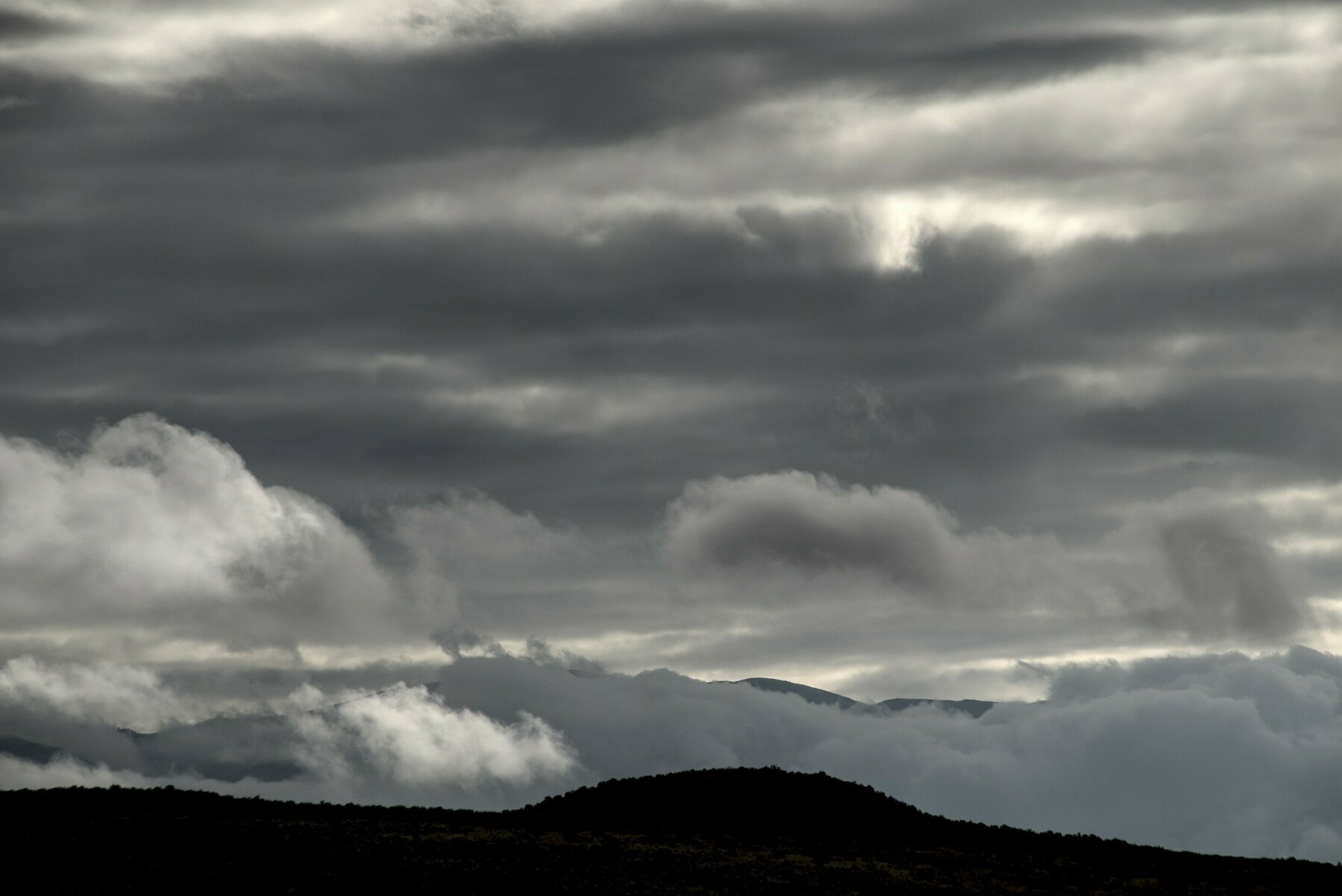 Clouds of varying size and greys cover the sky over mountains.