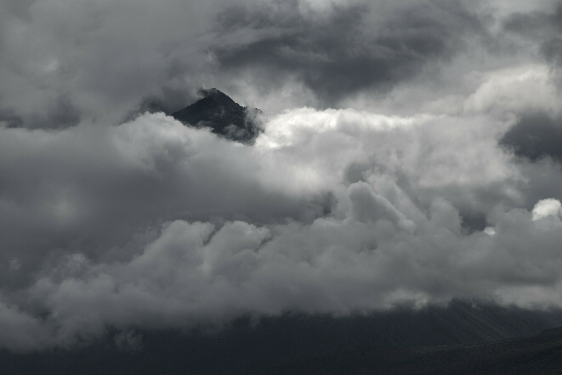Clouds obscure a mountain, with only its peak showing.