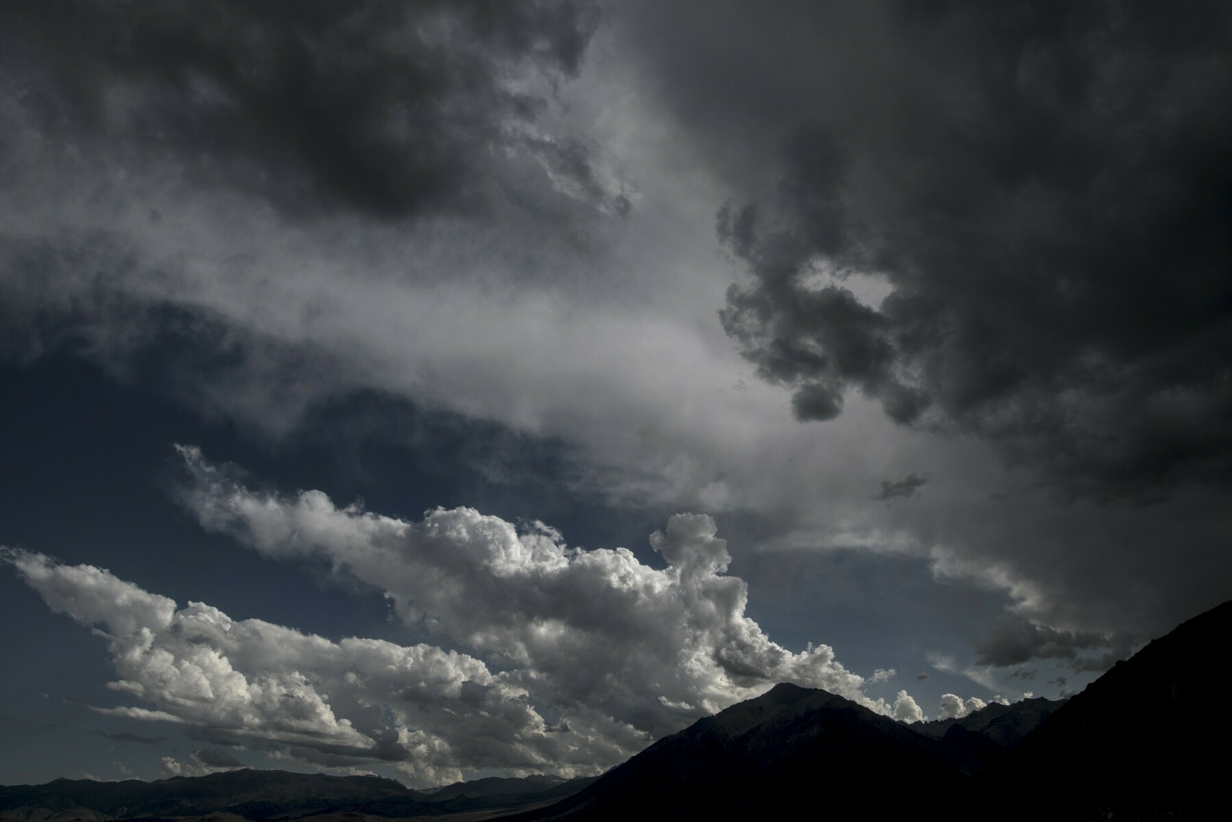 A large storm comes from the right over a high mountain, while blue sky and fluffy white clouds retreat to the left.