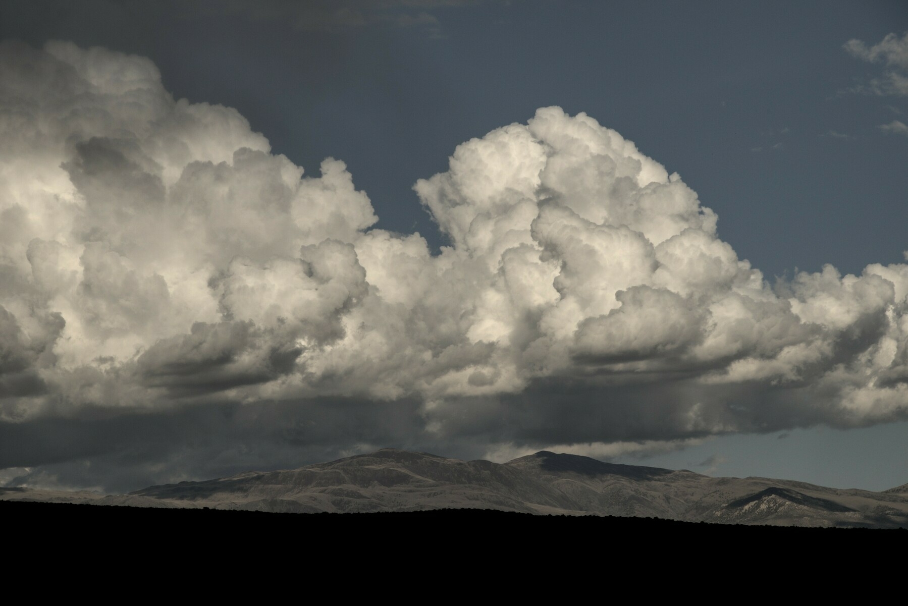 A long fluffy white cloud  hovers over a long mountain range.