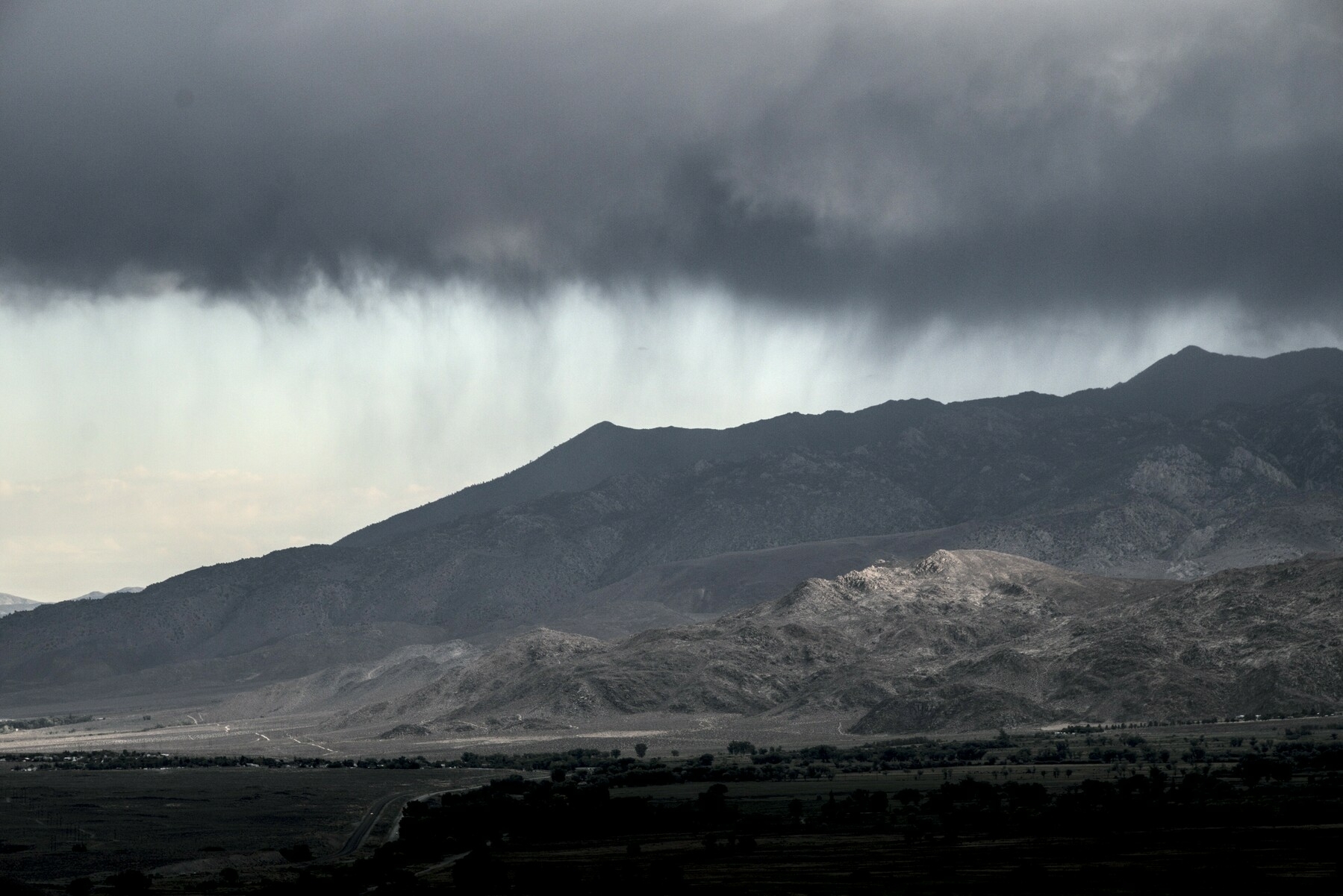 A bank of rain clouds hovers over a mountain valley in the distance.