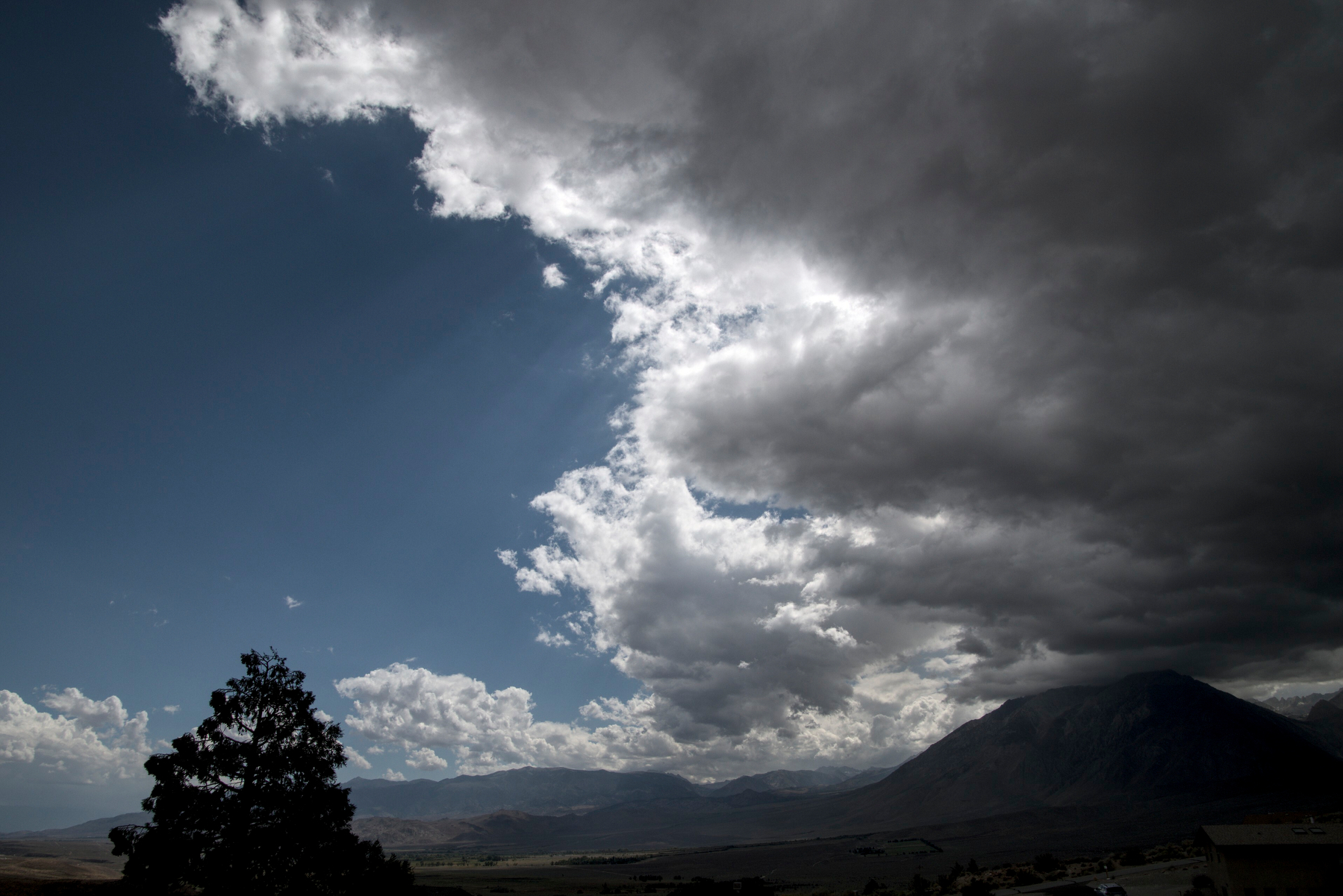 Storm clouds form an arc over a mountain valley, blue sky to the left, clouds to the right.