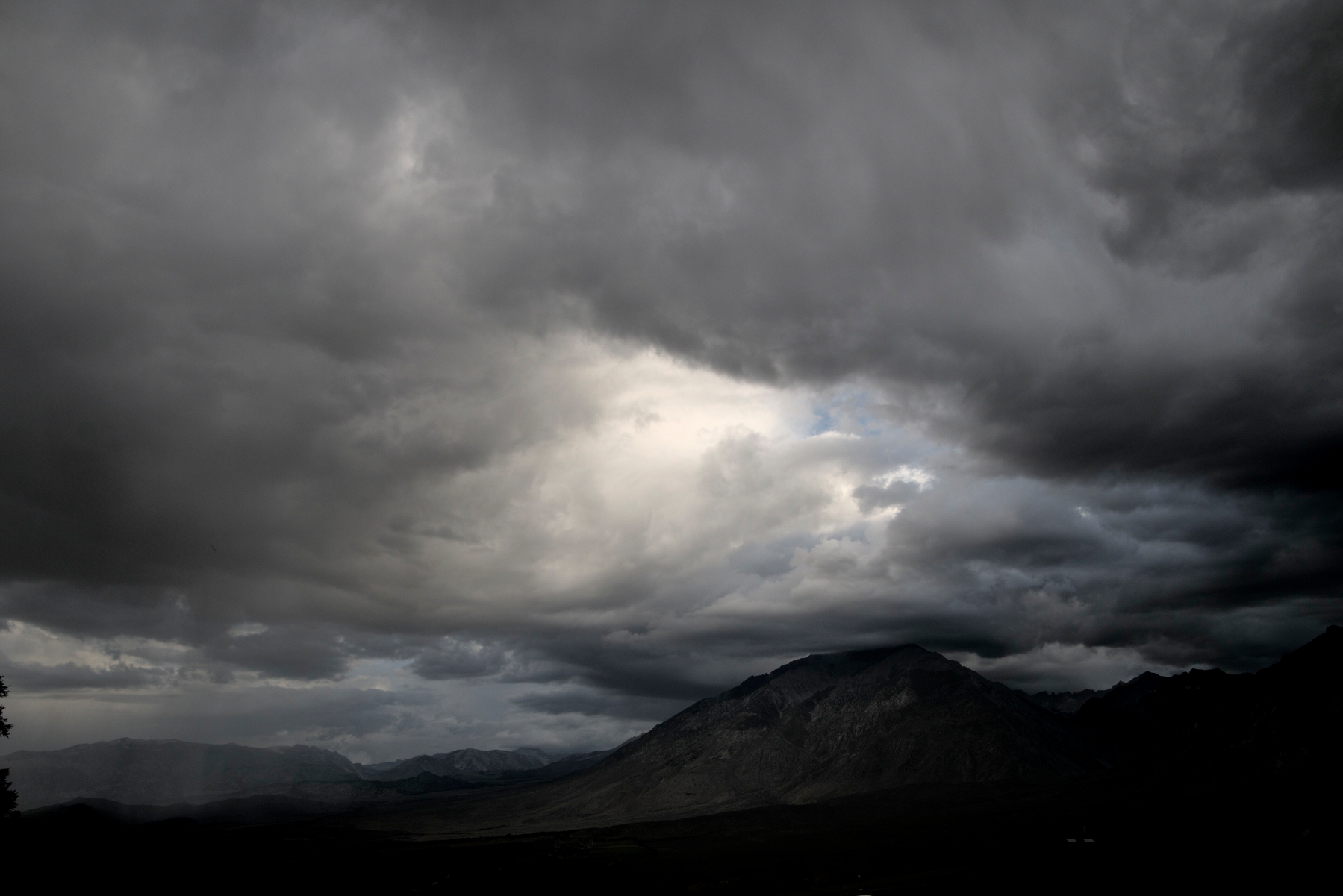 Dark clouds cover a mountain valley, but a gap in the center of the clouds lets light through.