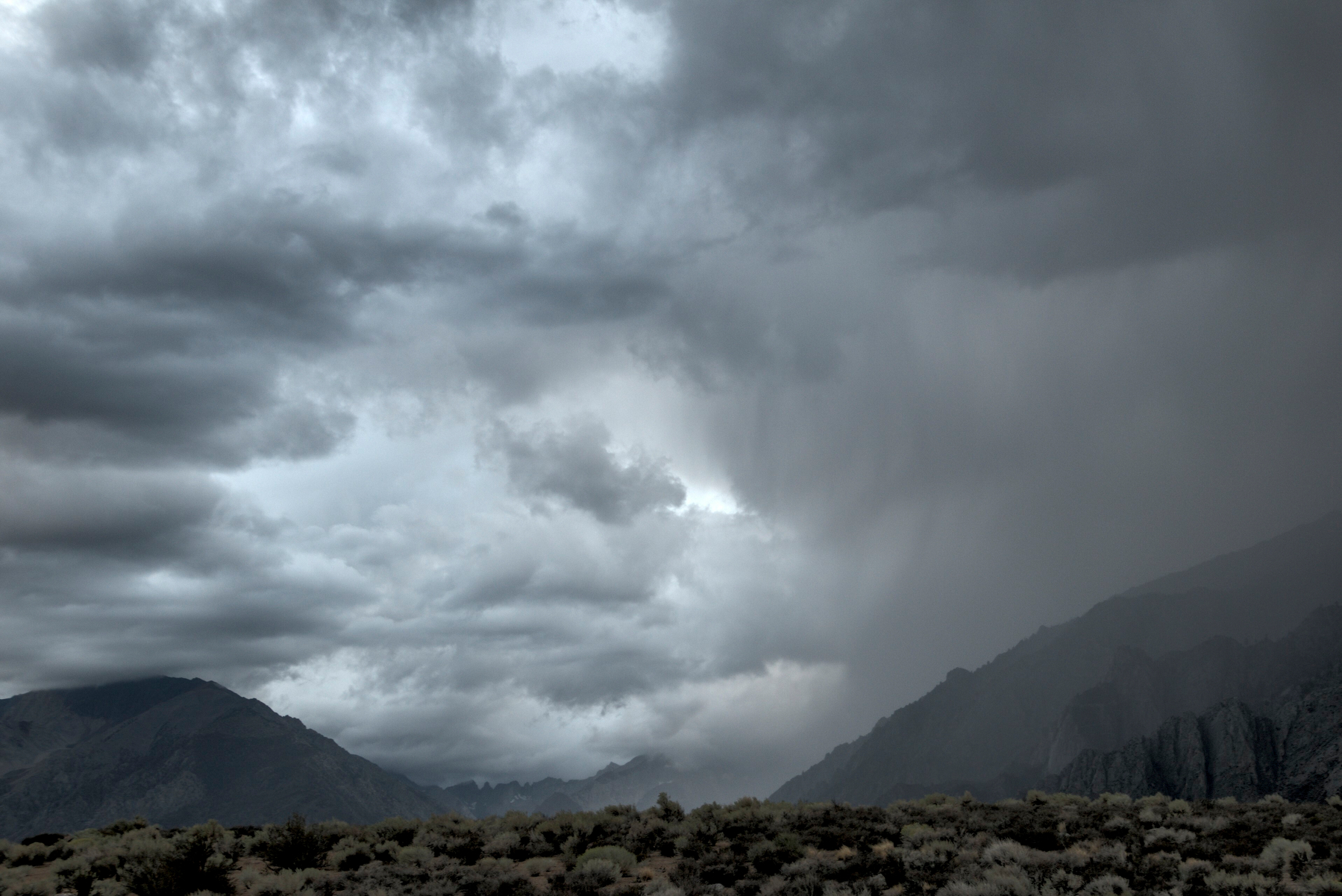 Storm clouds of varying darkness hover over high mountains separated by a deep canyon.