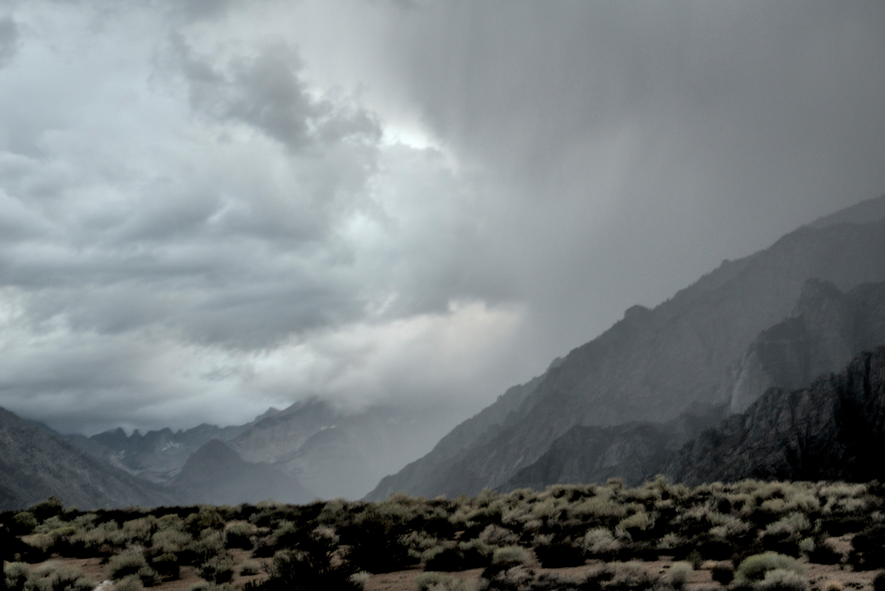 Dark clouds form over  mountain ridge, breaking up as they move over the adjacent valley.