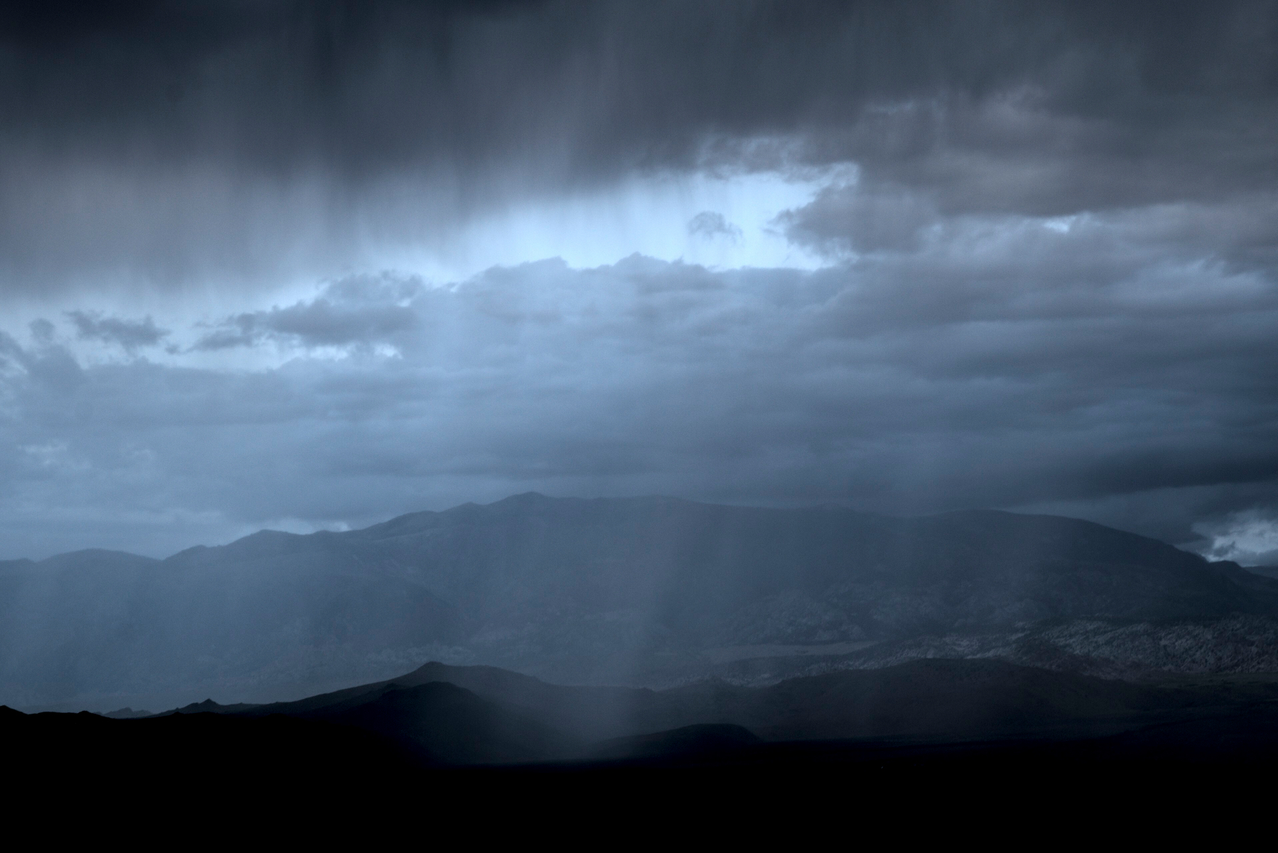 Rain falls in the distance from a layer of dark clouds over mountains, forming a veil.