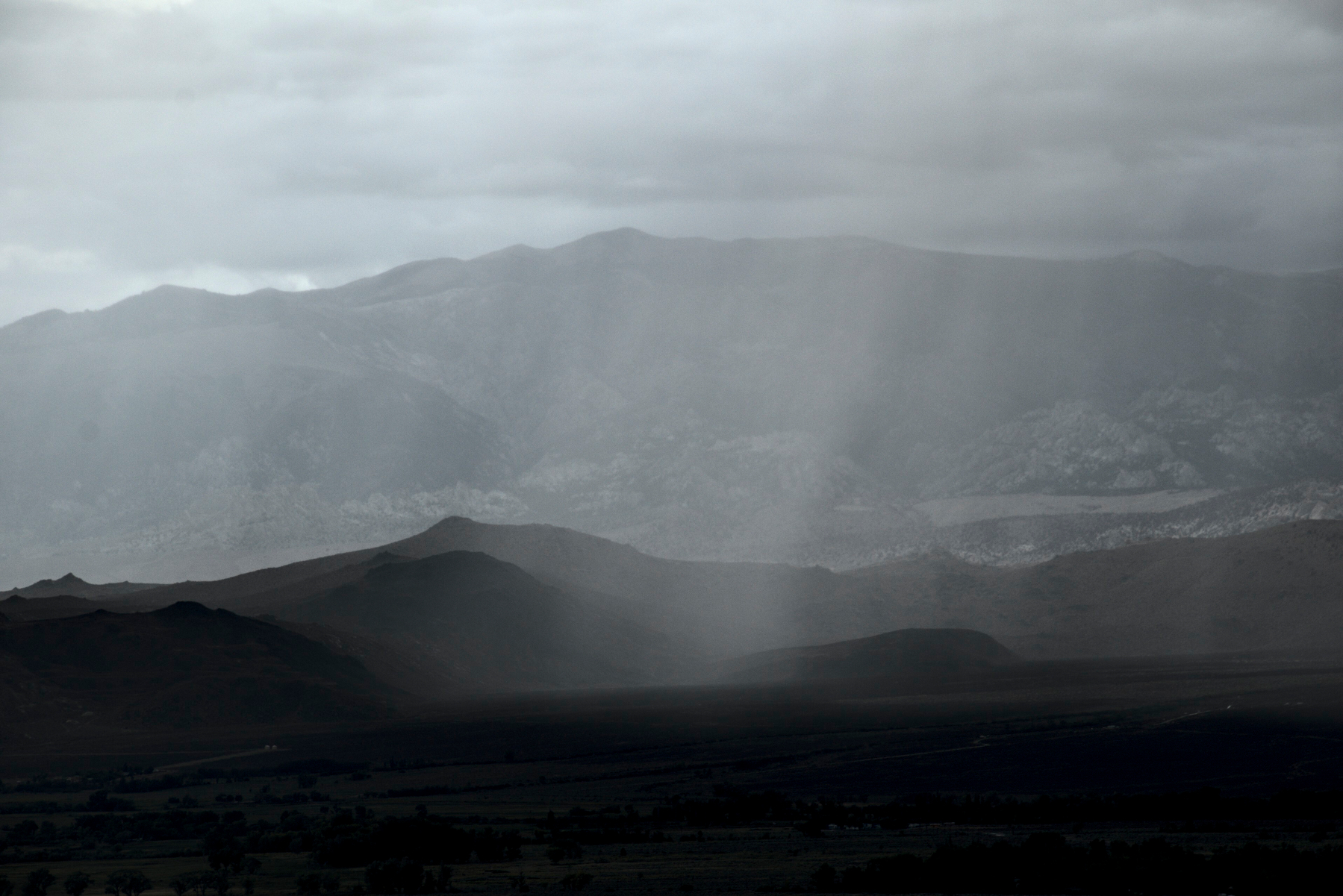 Rain falling from dark clouds forms a veil over a mountain valley.