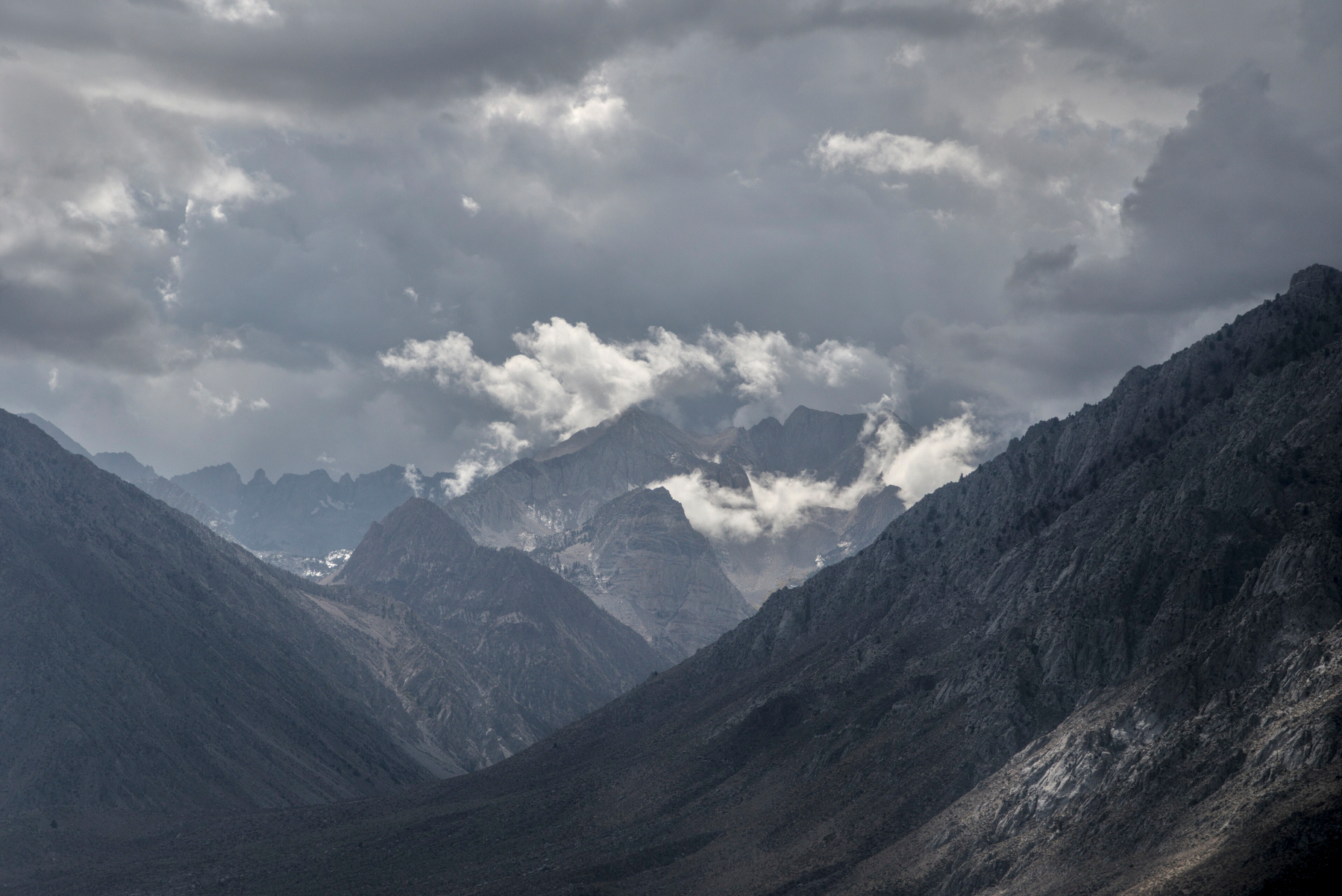 A mountain valley leads to another mountain in the distance, which has a wreath of small clouds around the top.