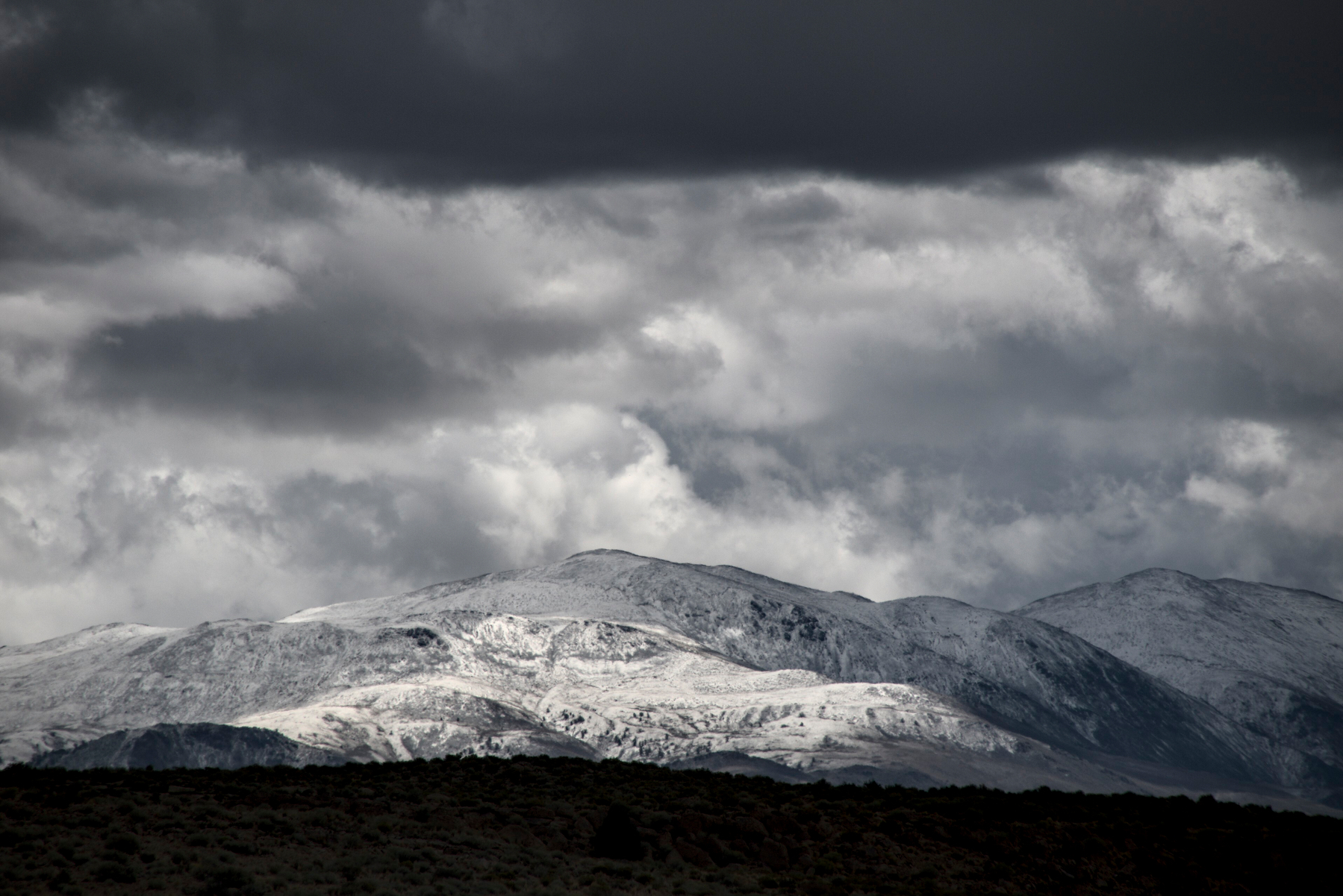 A high mountain has fresh snow, with a layer of dark clouds above.
