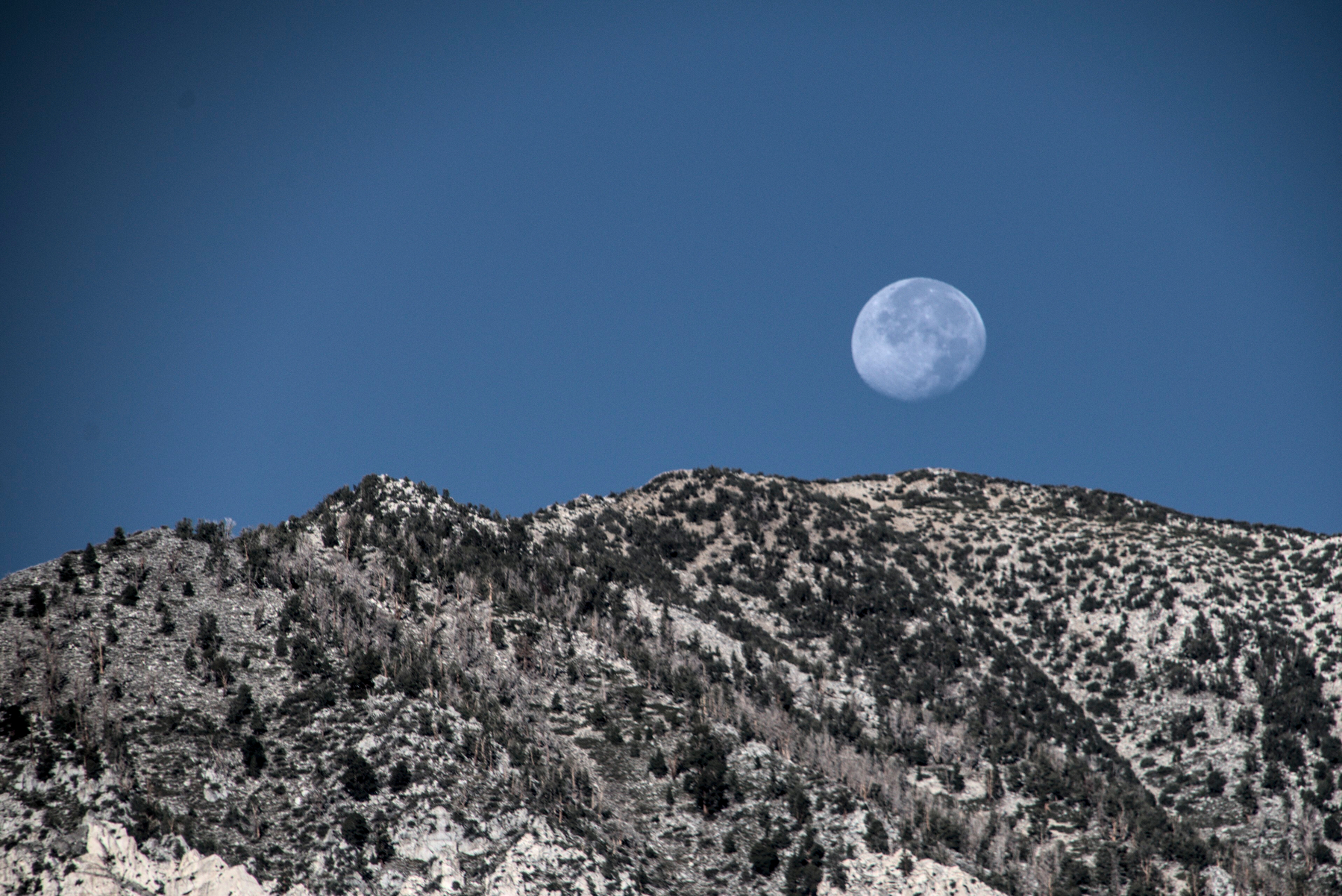 A full-ish moon sits just above a granite ridge.