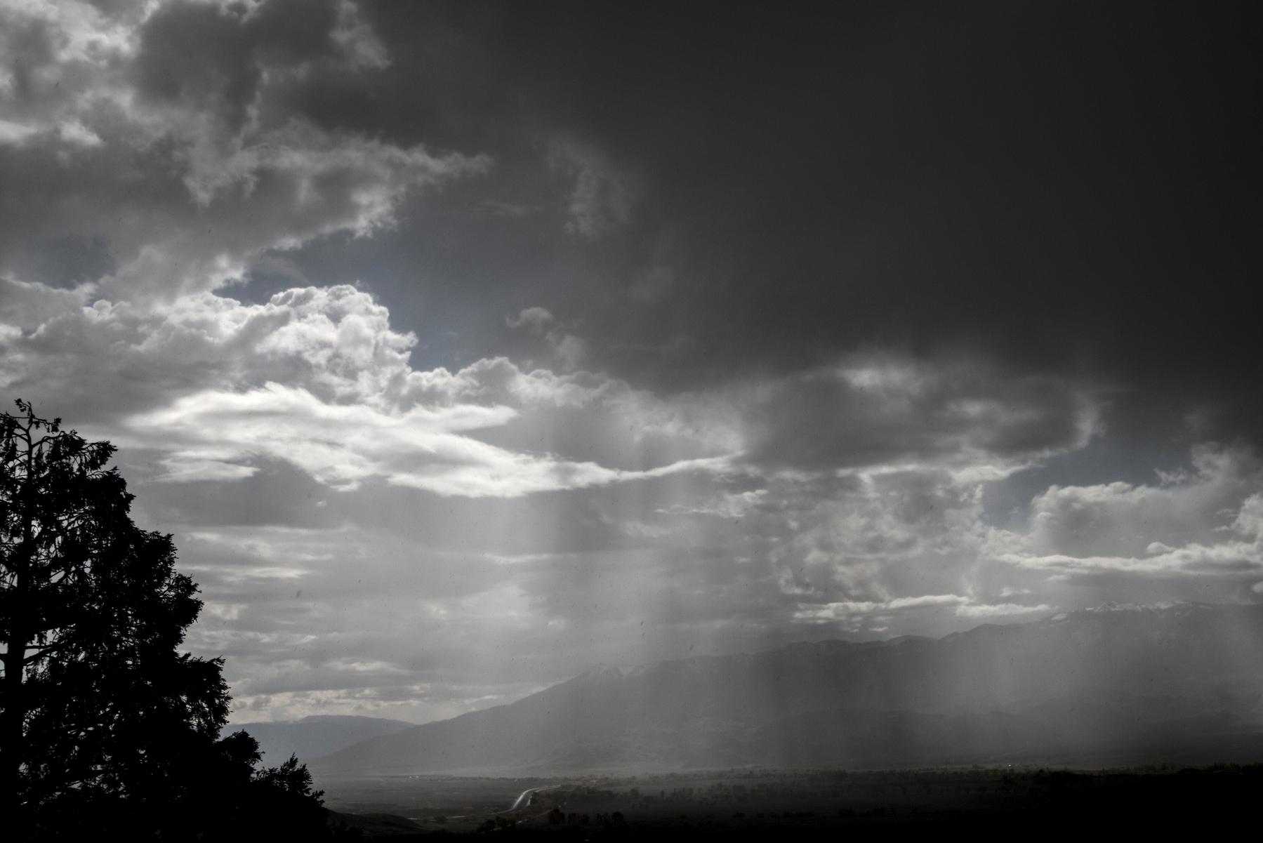 A high desert valley has blue skies to the left, dark cloud and rain to the right, with rain falling in the middle.