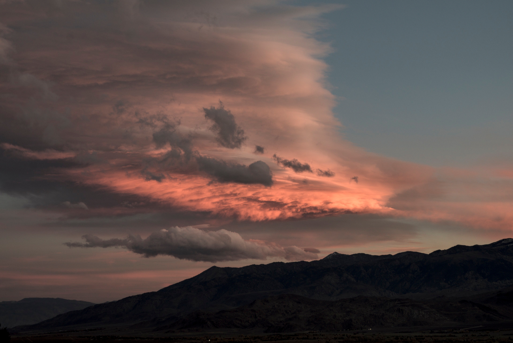 Pink and grey clouds over mountains at sunset.