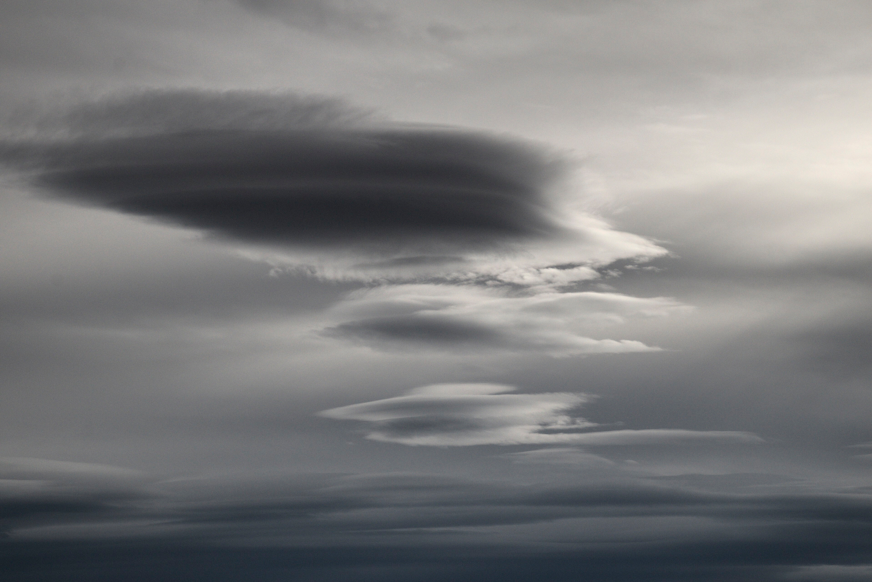 Lenticular clouds in a vertical stack, grey against a grey sky.