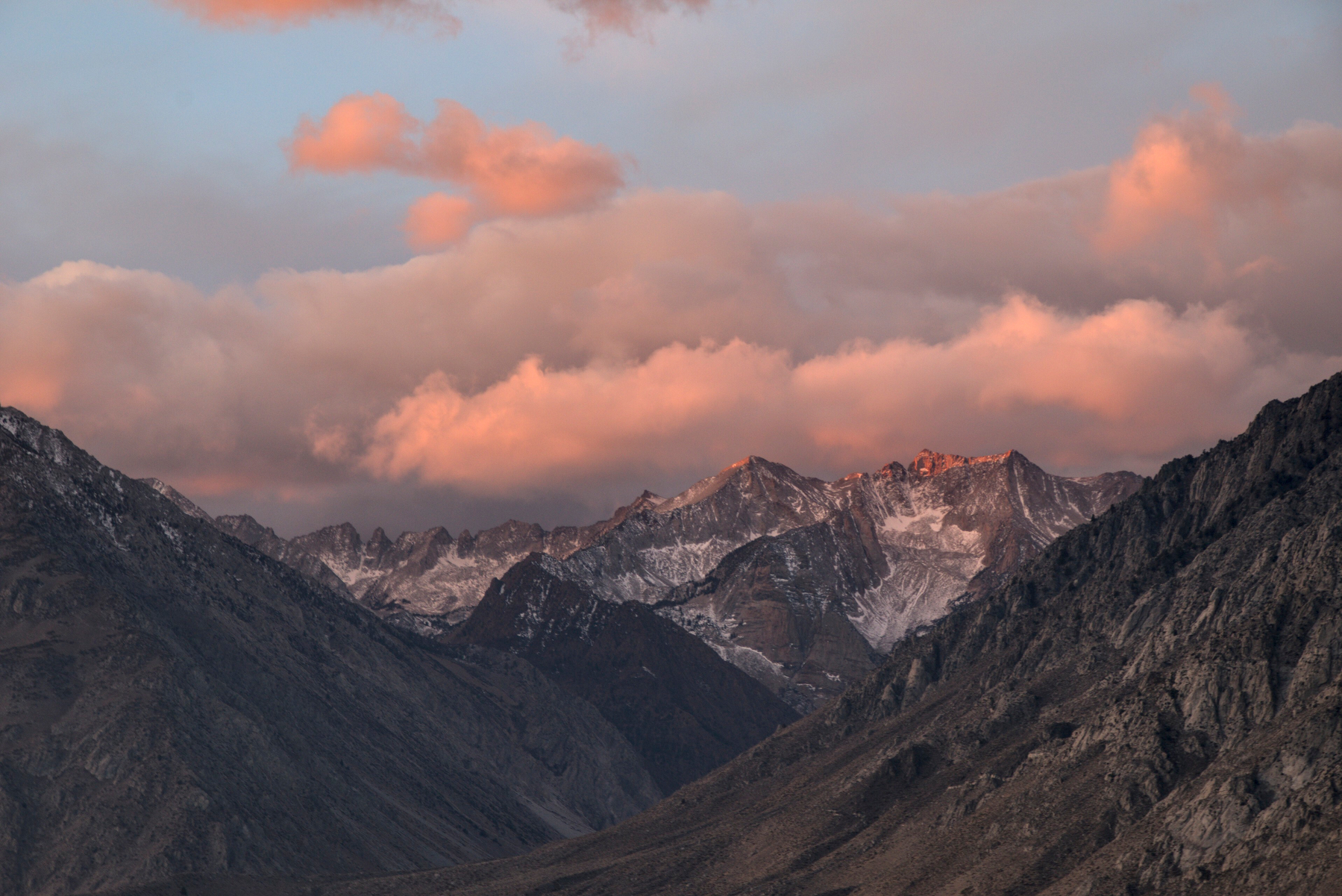 Mountains at the far side of a valley are covered by pink clouds.