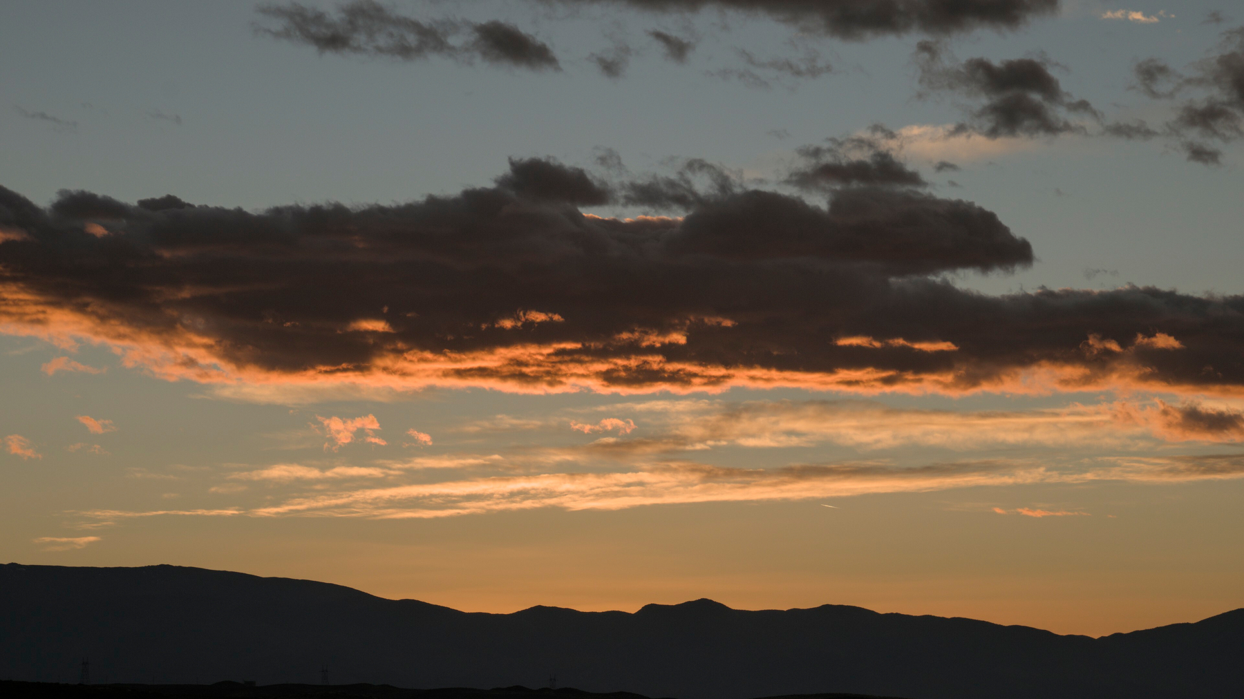 Clouds over mountains to the east are backlit by the rising sun.