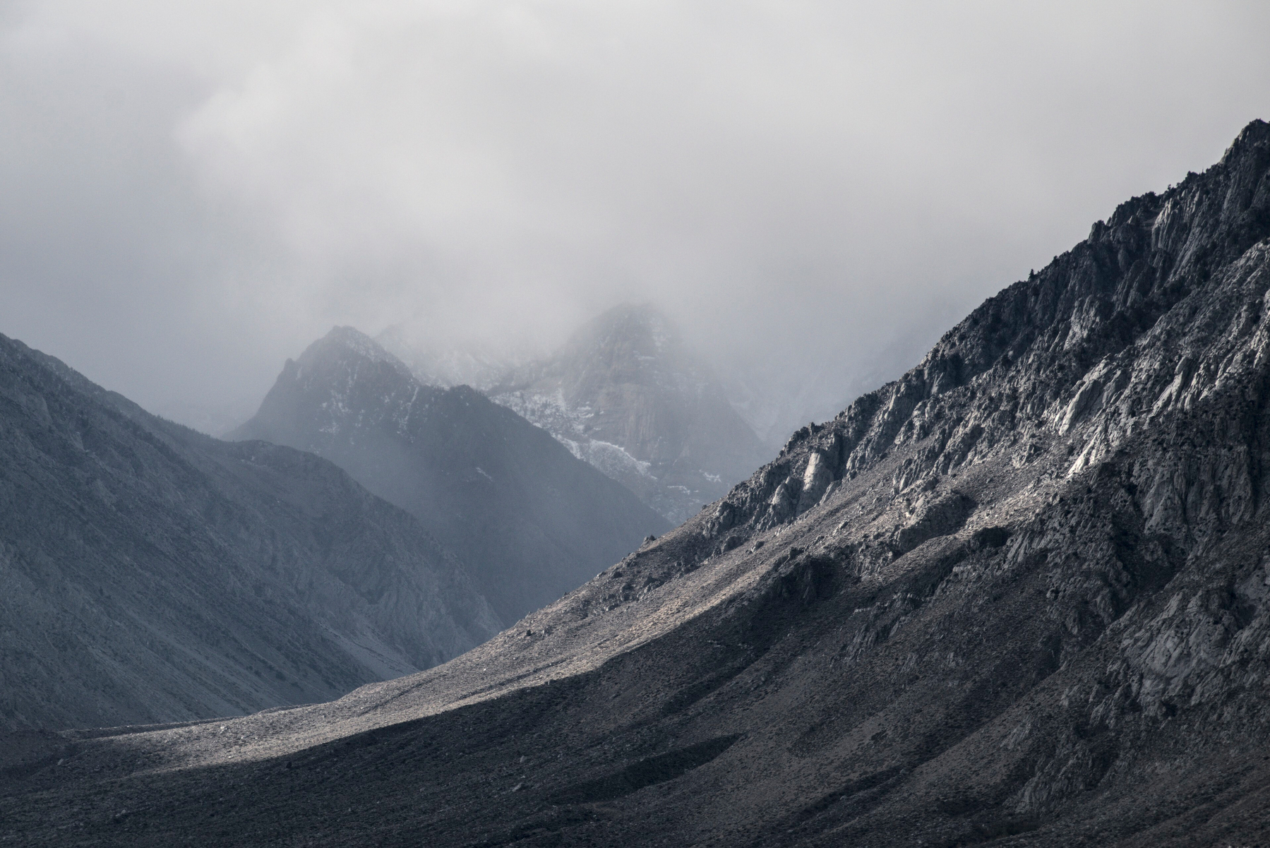 A mountain ridge lit by sunlight slopes down from the right, while mountains and storm fill the background.