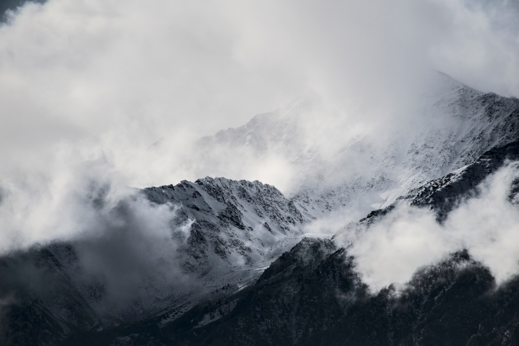 A mountain peak of rough granite is half obscured by clouds clinging to it.