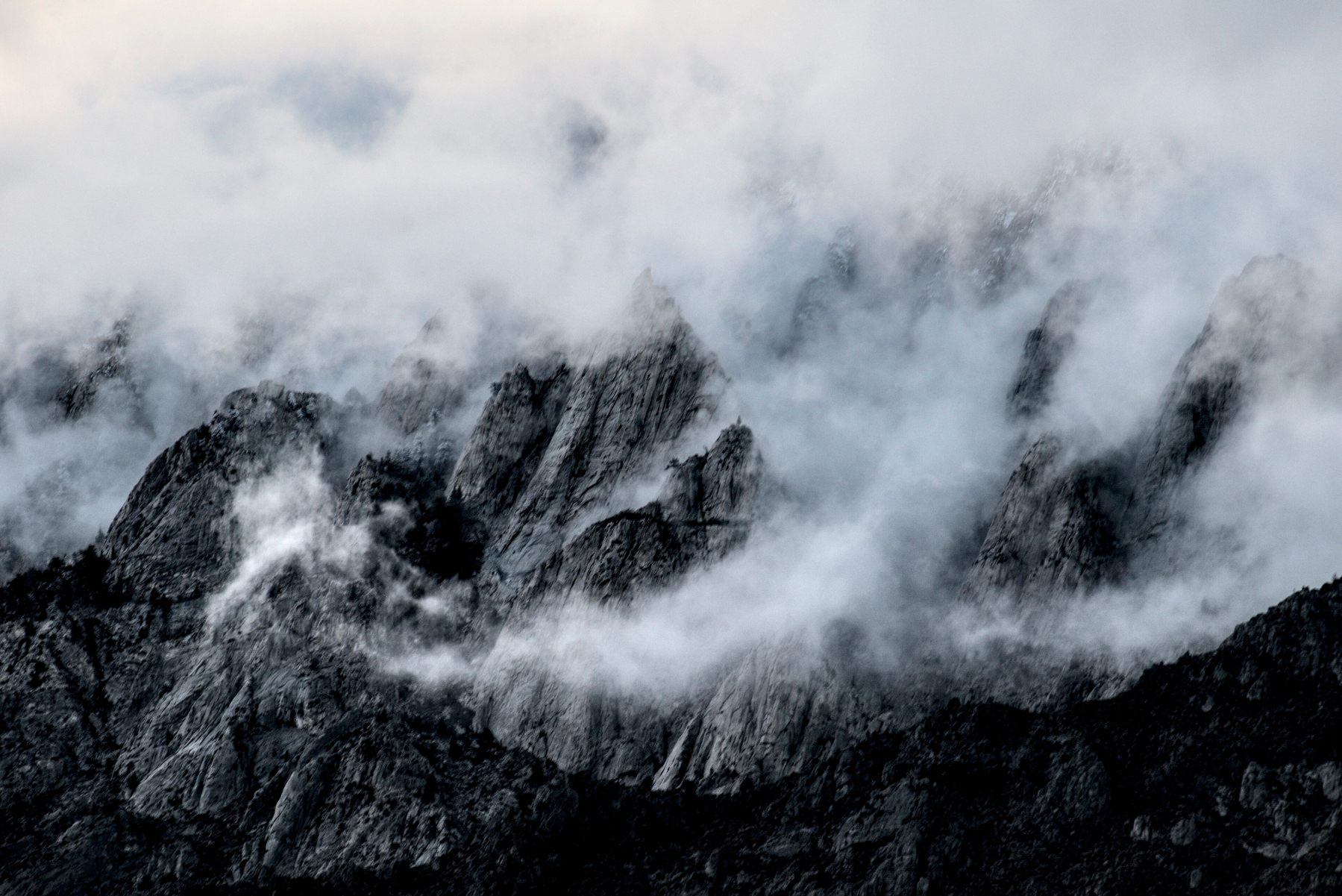 A craggy granite rock face is partially obscured by tendrils of fog.