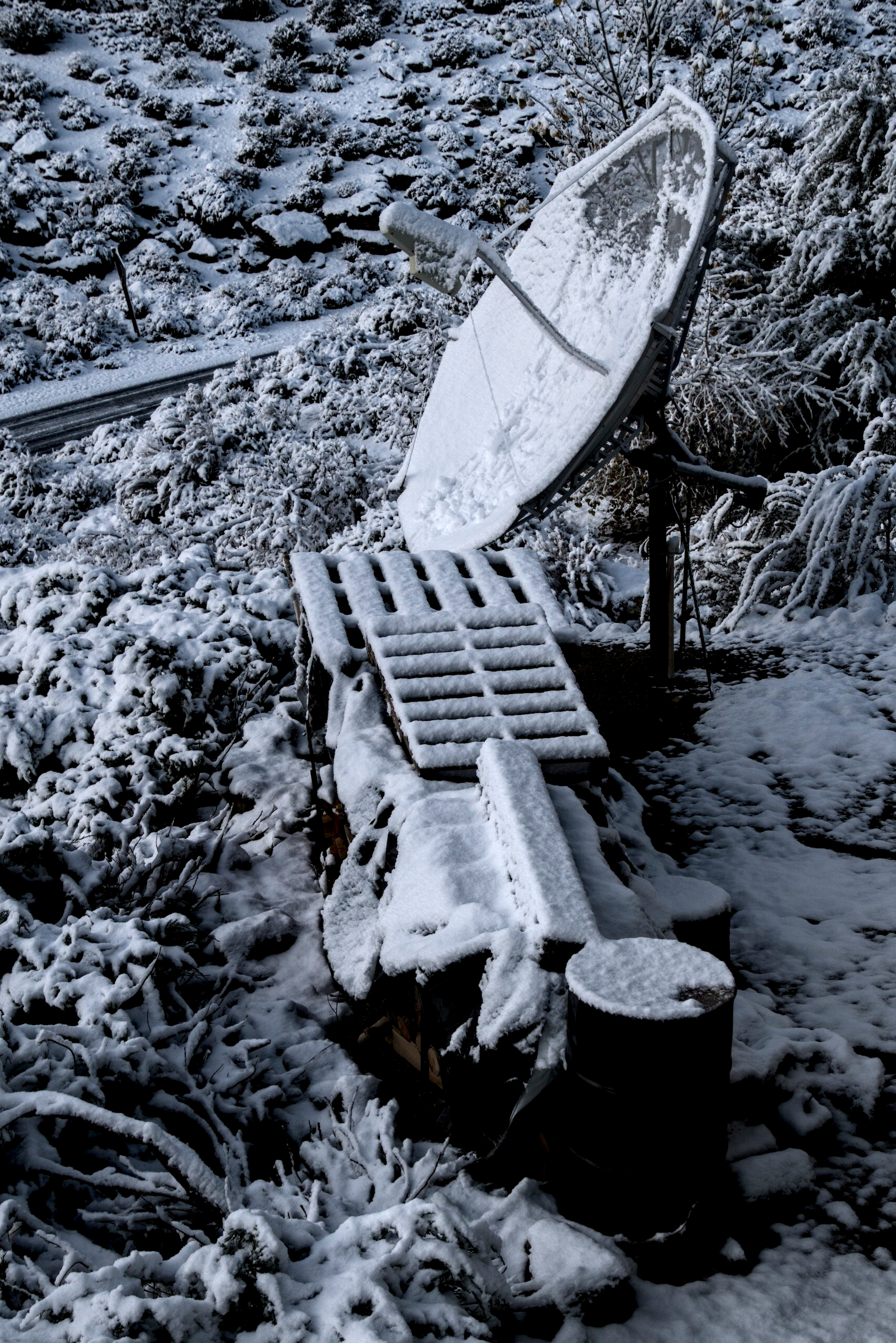 Snow covers a satellite dish and some shipping palettes.
