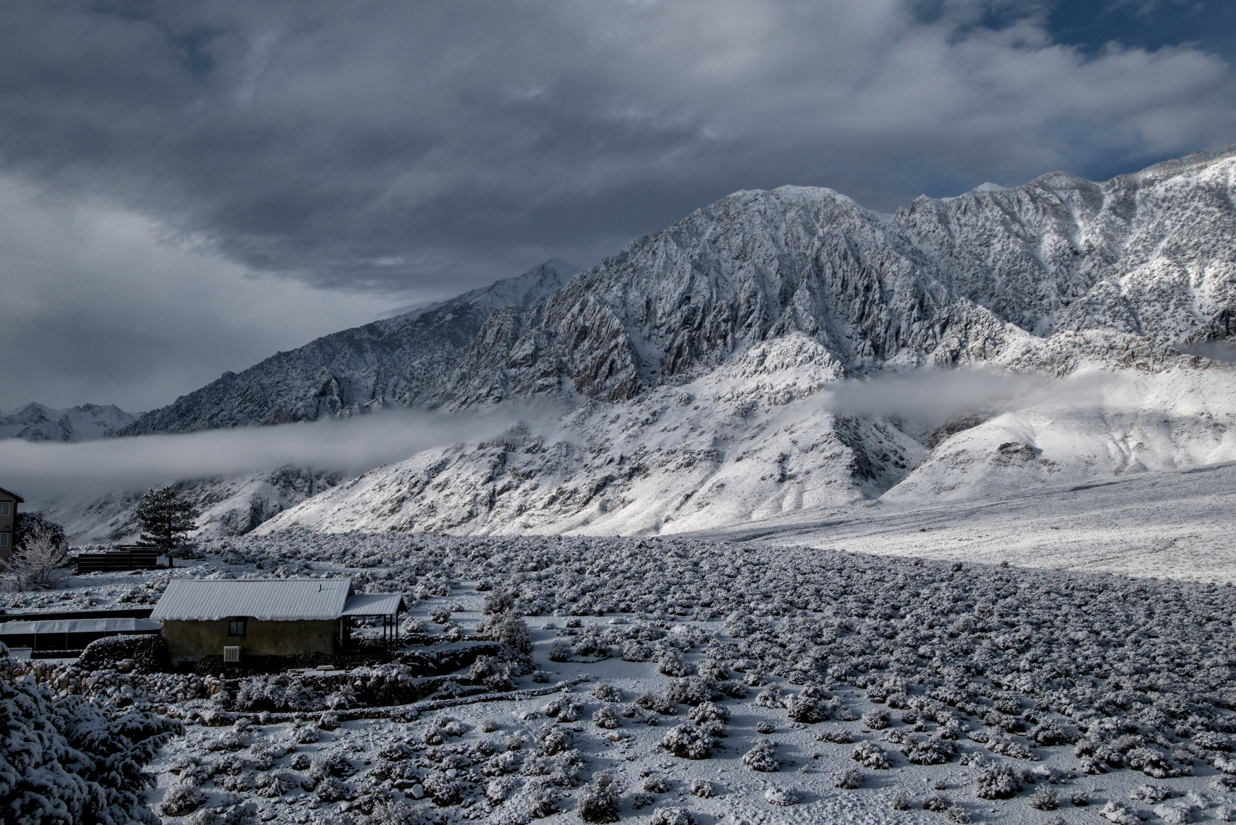 A small house looks out on a snow covered mountainous wilderness.