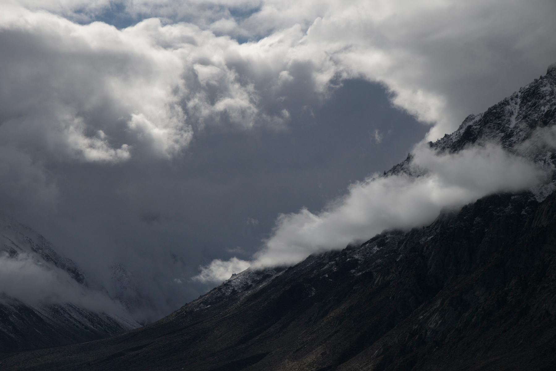 Bright clouds overhang a mountain canyon, where the air is clear and dark inside.